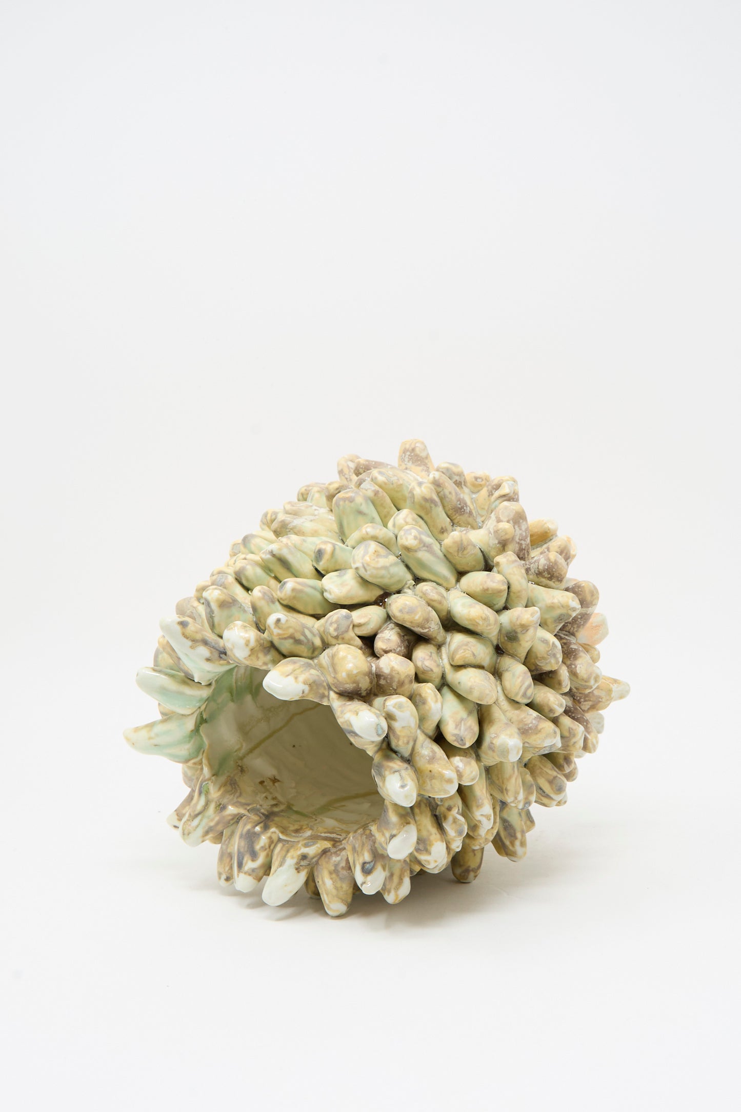 The MONDAYS Soda-Fired Rasmus Bump Vase is a handmade porcelain vessel with an open sculptural form, featuring numerous pointed, textured light green and beige protrusions, displayed against a plain white background.