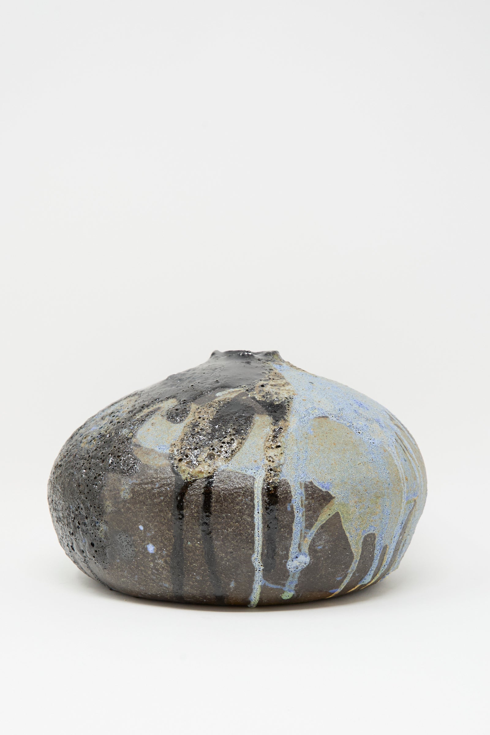 The MONDAYS Textured Moon Vase in Black is a handmade round vase with a small opening, featuring a dark textured surface and multicolored blue, white, and gray glaze drips that stand out against a plain white background.