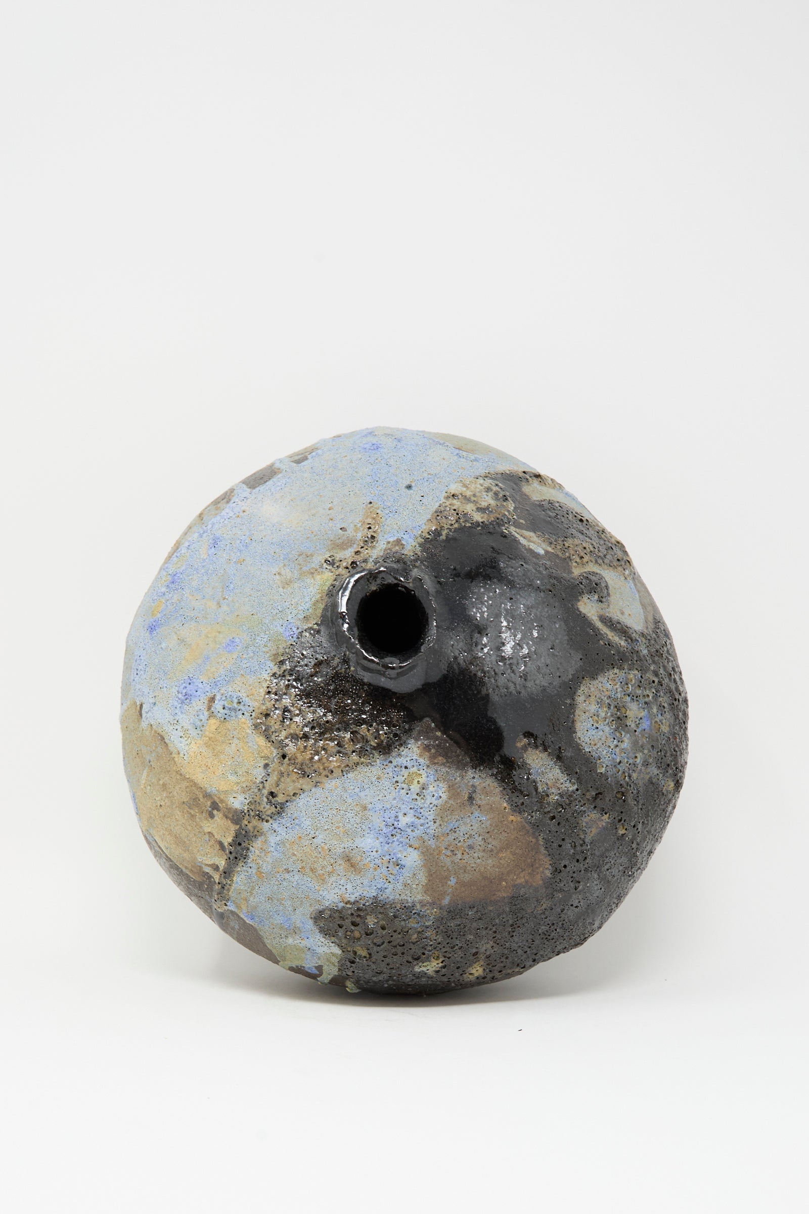 The MONDAYS Textured Moon Vase in Black is a round, handmade piece with a small off-center opening, combining matte blue, tan, and glossy black finishes. Its unique texture stands out against a plain white background.