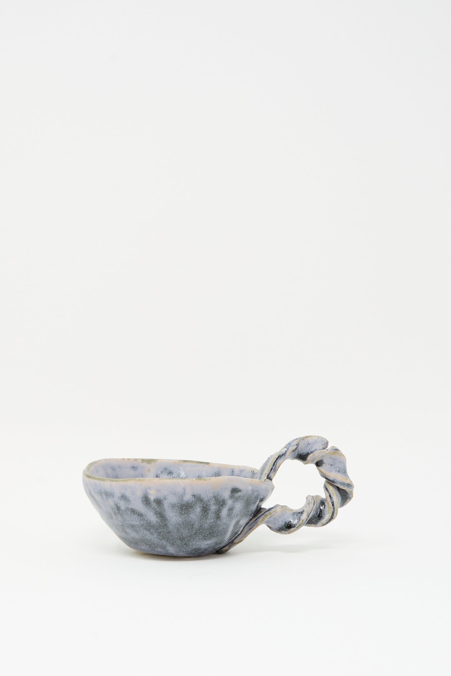 The Twist Teacup in Blue by MONDAYS features a unique twisted handle and blue-gray glaze, crafted in Brooklyn. Shown here against a plain white background.
