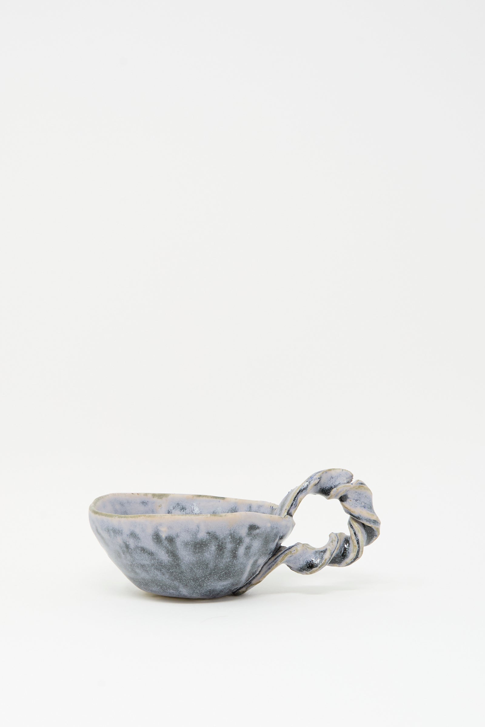 The Twist Teacup in Blue by MONDAYS features a unique twisted handle and blue-gray glaze, crafted in Brooklyn. Shown here against a plain white background.