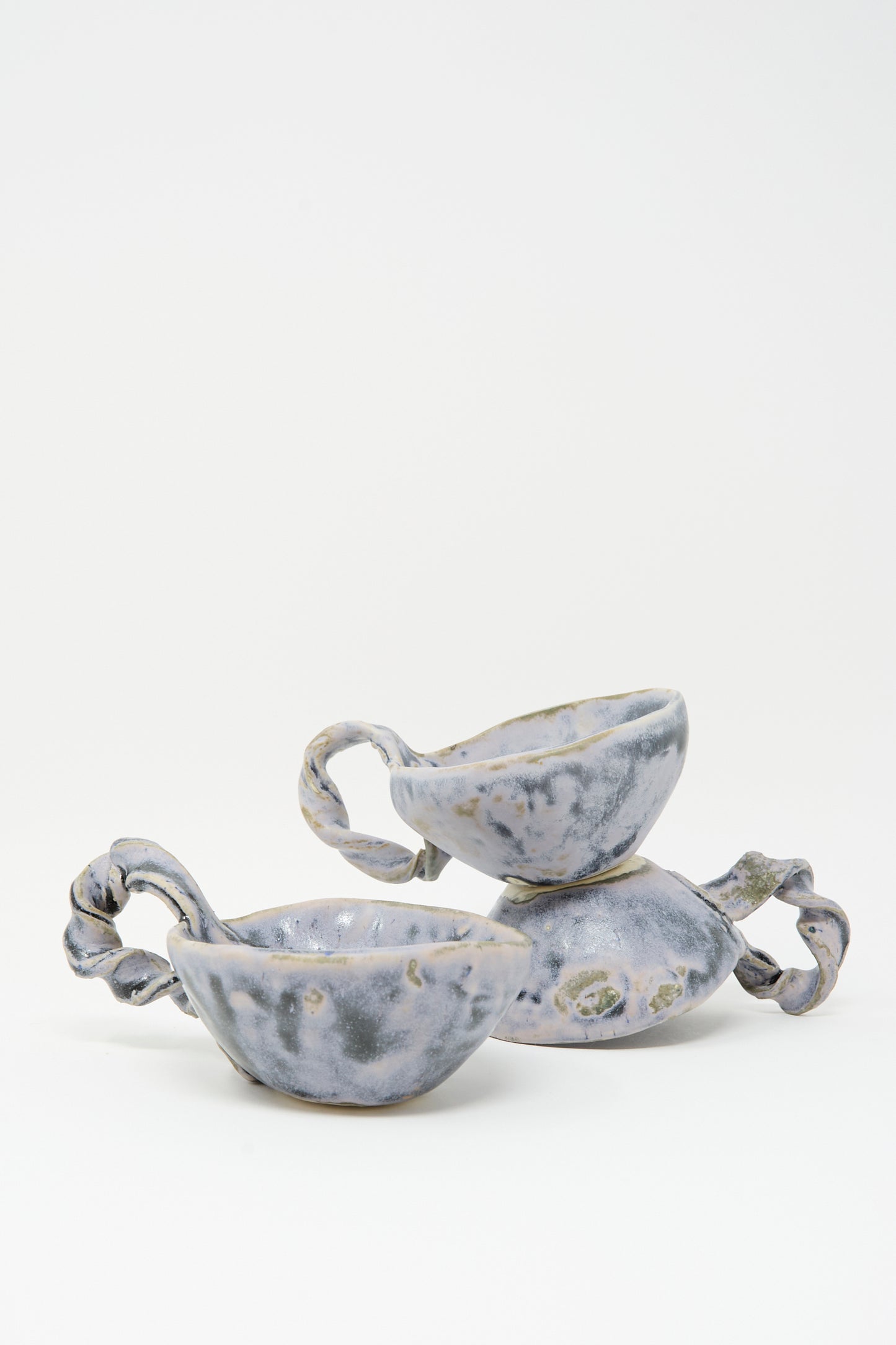 Two MONDAYS Twist Teacups in Blue, featuring irregular textured surfaces and twisted handles, are stacked against a plain white background, highlighting Brooklyn craftsmanship.