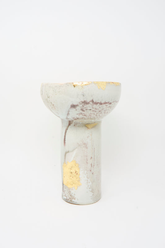 The MONDAYS Wood-Fired Porcelain Pedestal Bowl with Gold Leaf features a tall cylindrical base, a wide bowl top, white glaze, gold leaf accents, and subtle brown marbling.