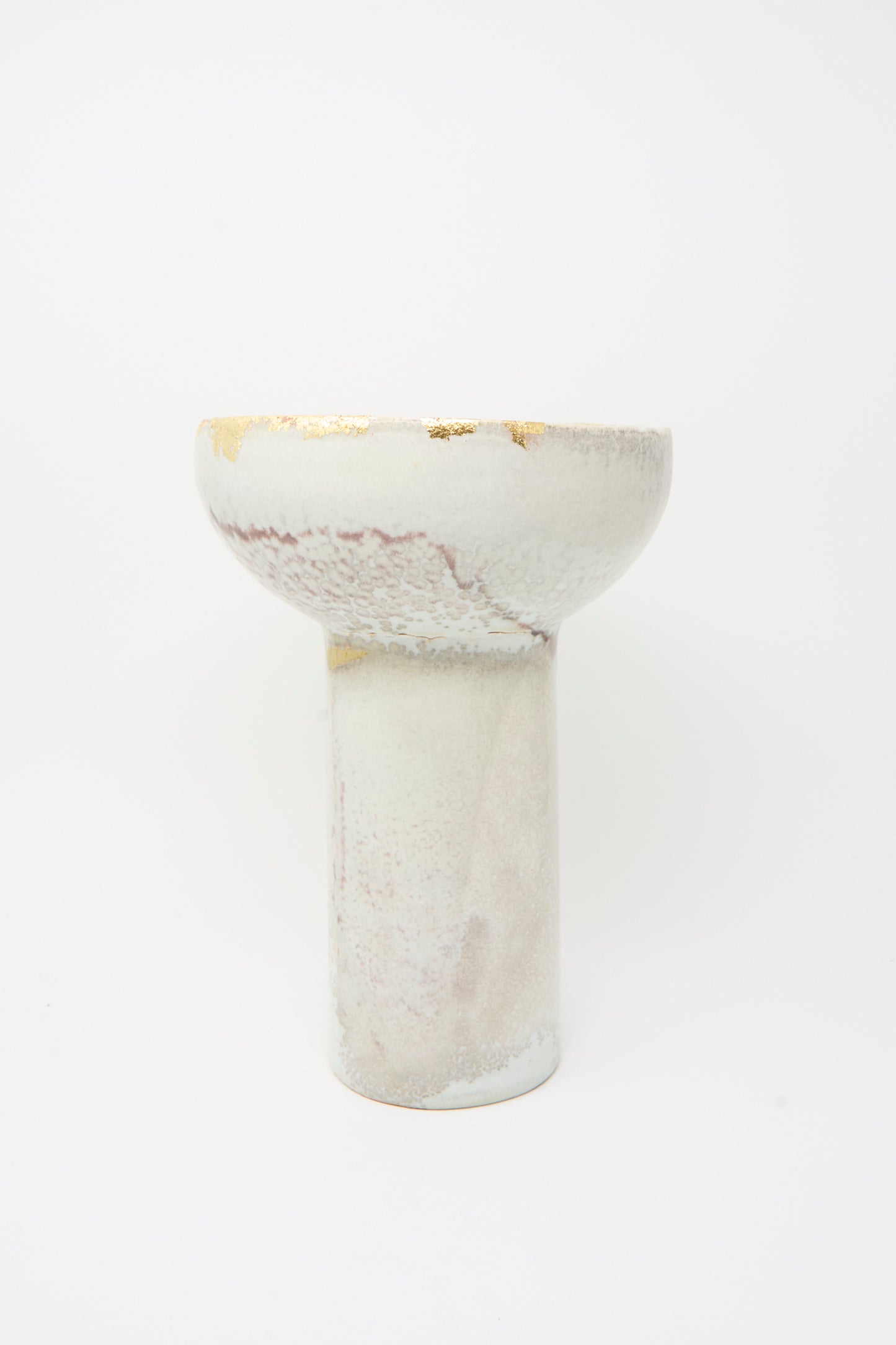 The MONDAYS Wood-Fired Porcelain Pedestal Bowl with Gold Leaf has a tall cylindrical base, a wide rounded top, and features a light marbled glaze with gold leaf detailing.