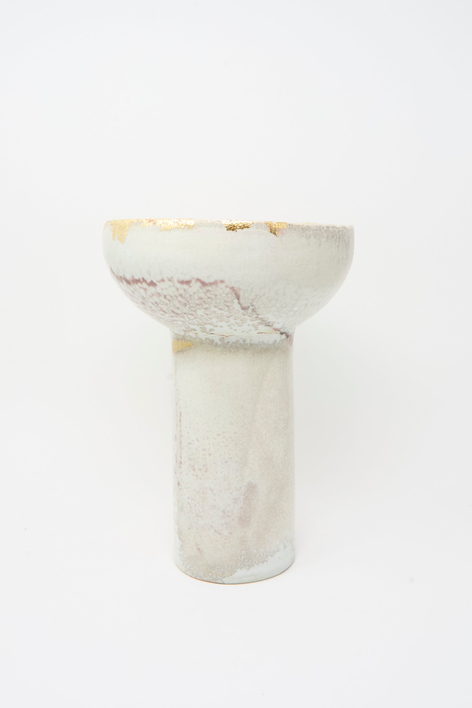 The MONDAYS Wood-Fired Porcelain Pedestal Bowl with Gold Leaf has a tall cylindrical base, a wide rounded top, and features a light marbled glaze with gold leaf detailing.