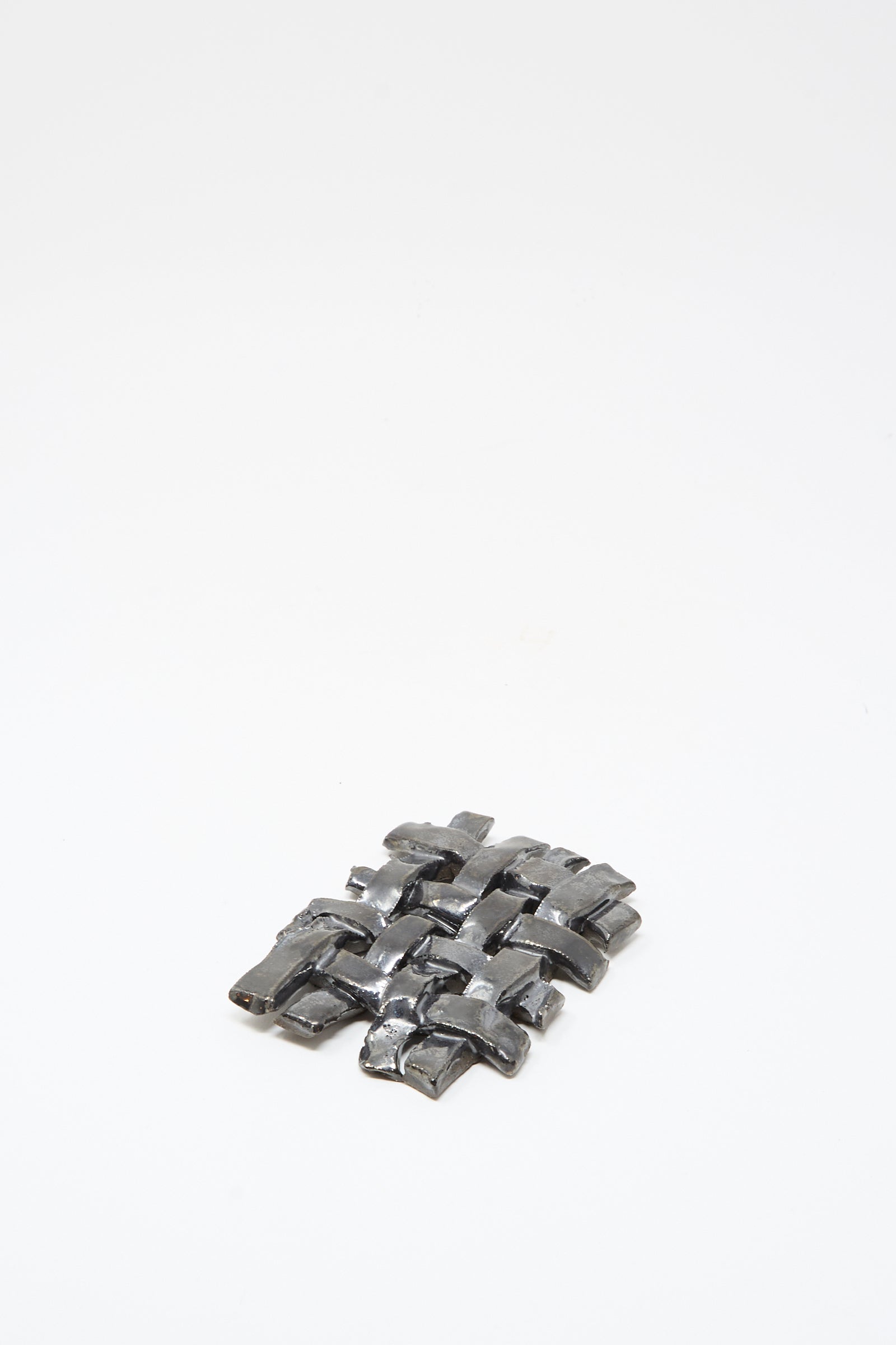 A small woven grid of shiny metal strips on a white background, resembling the MONDAYS Woven Dish in Charcoal.