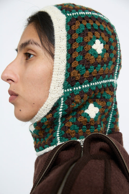 Person wearing the Maria La Rosa "Balaclava in Emerald," featuring a hand-knit geometric pattern with green, brown, and cream colors, against a white background. 