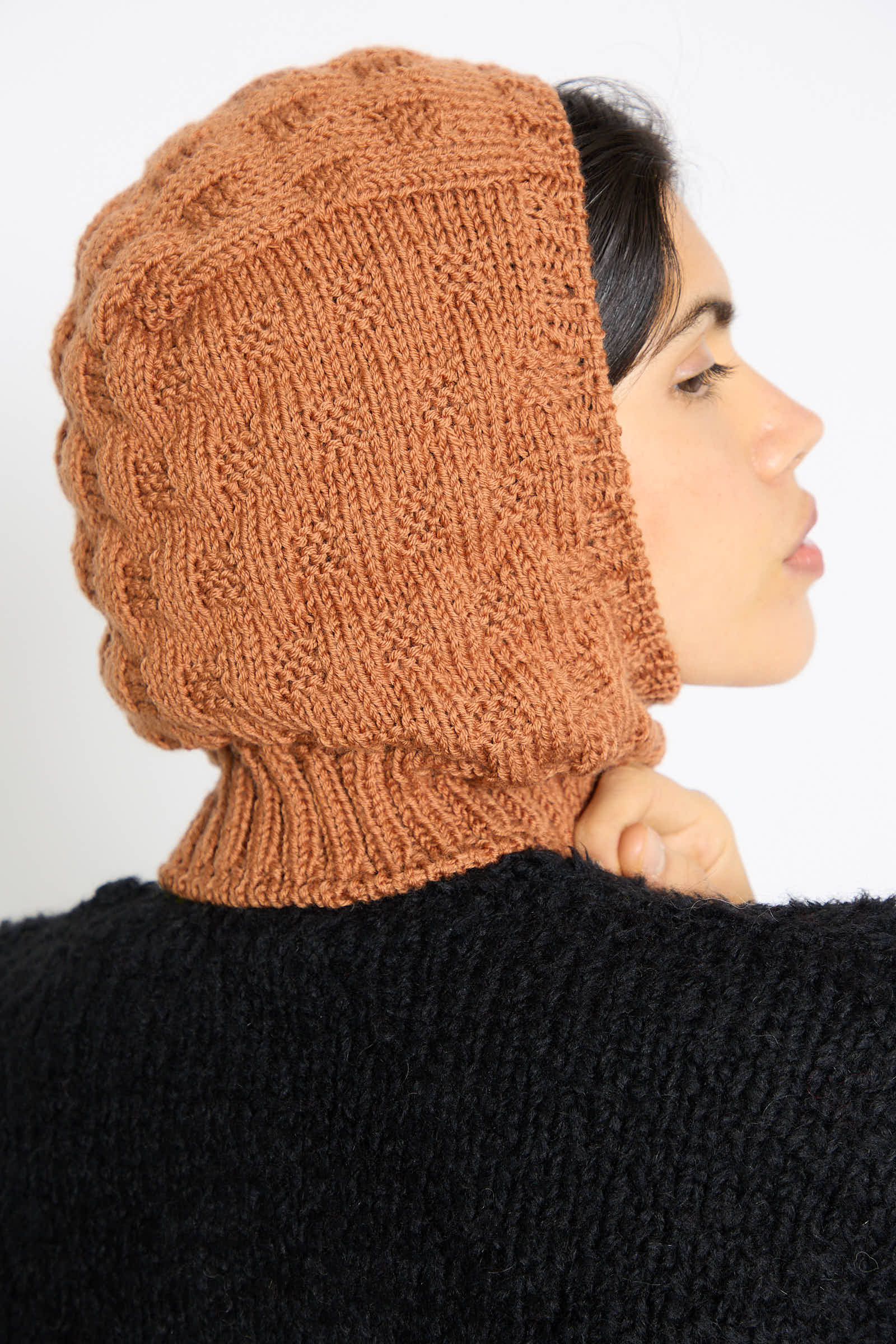 A person wearing Maria La Rosa's Balaclava in Rust and a black sweater, looking to the side.