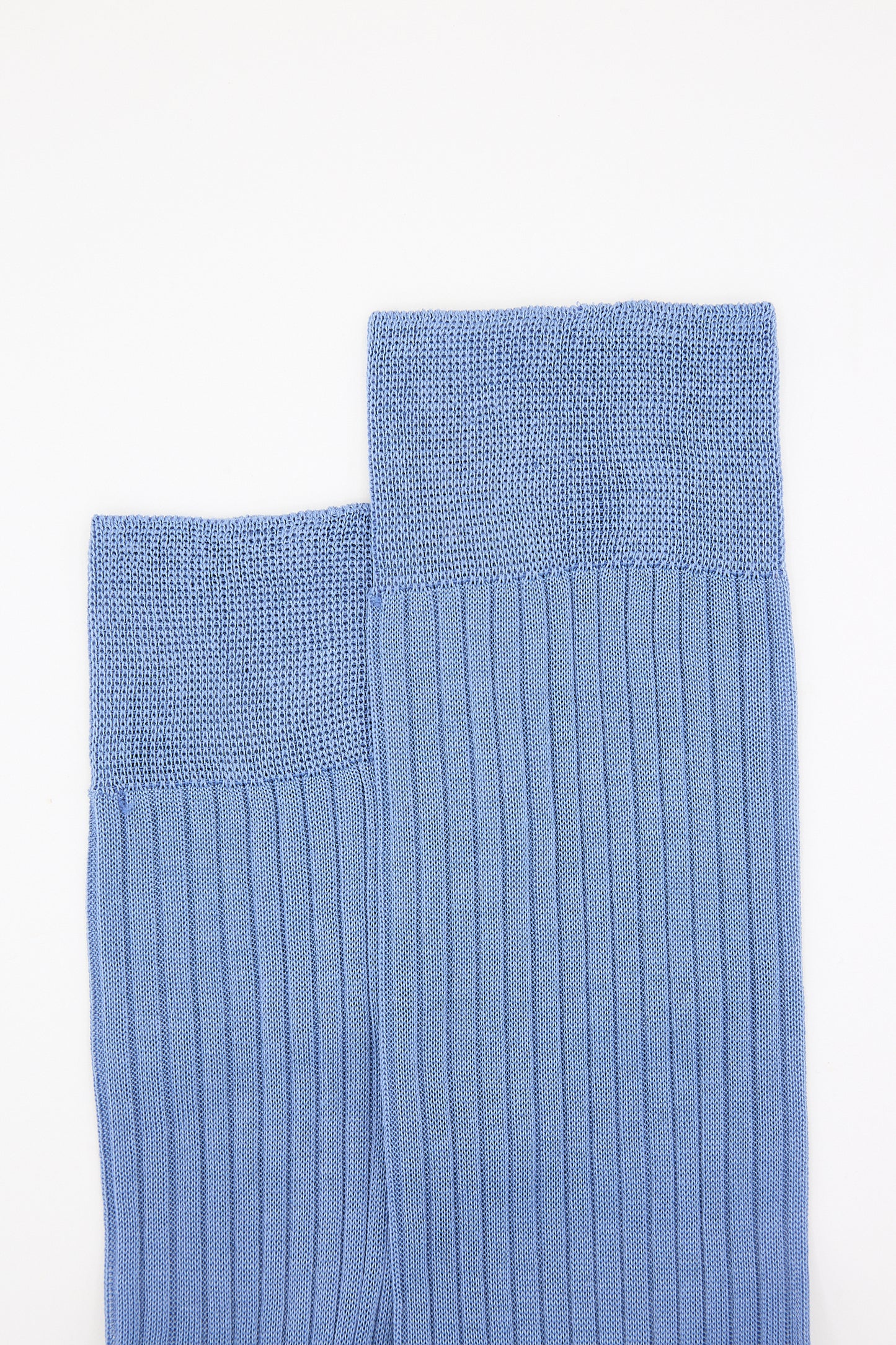Two folded blue knit sweaters and a pair of Maria La Rosa Rib Socks in Light Blue on a white background.