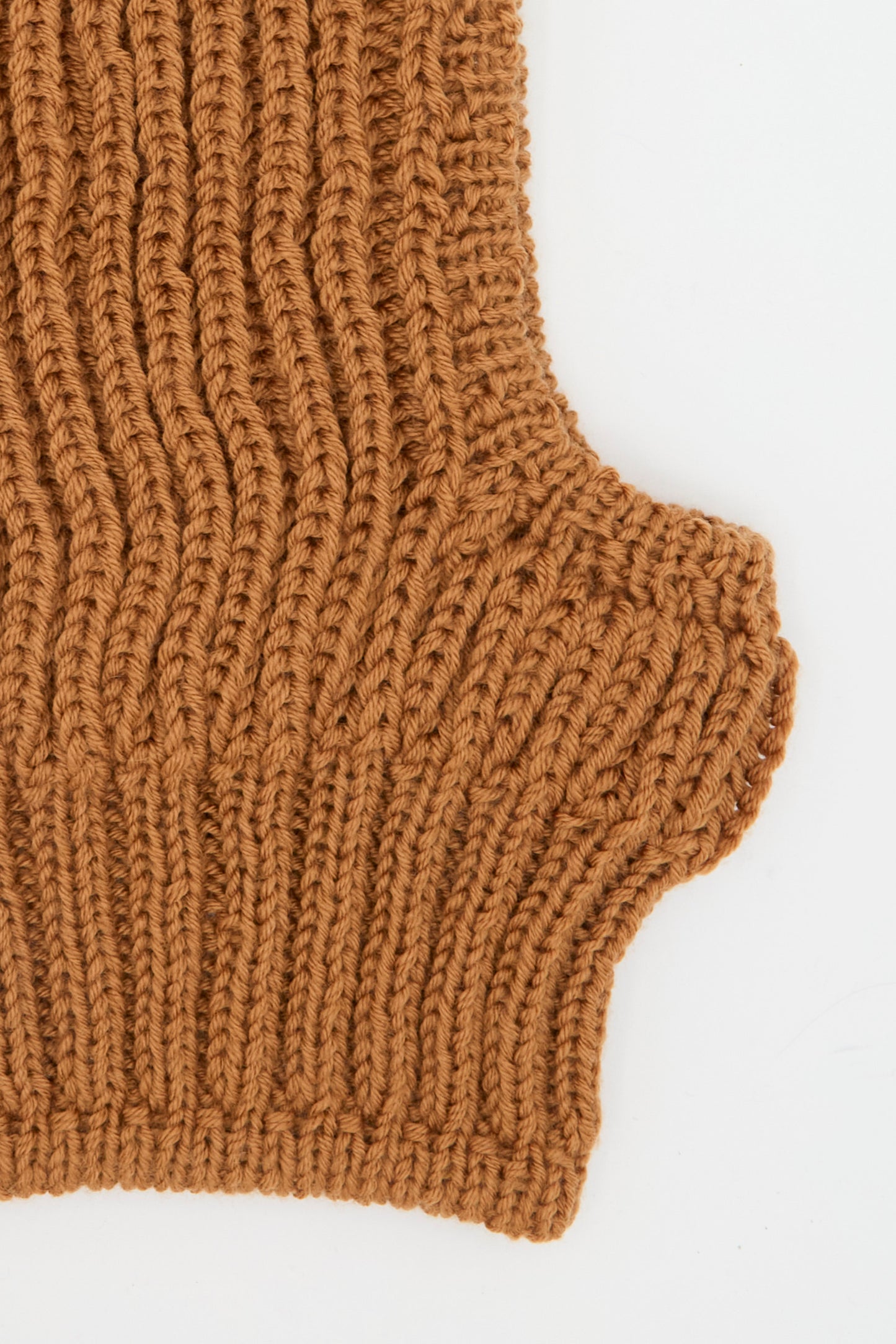 Close-up of rib knit wool fabric in rust, showing curved edge detail against a white background—part of the handmade Wool Balaclava Lina by Maria La Rosa, crafted in Italy.