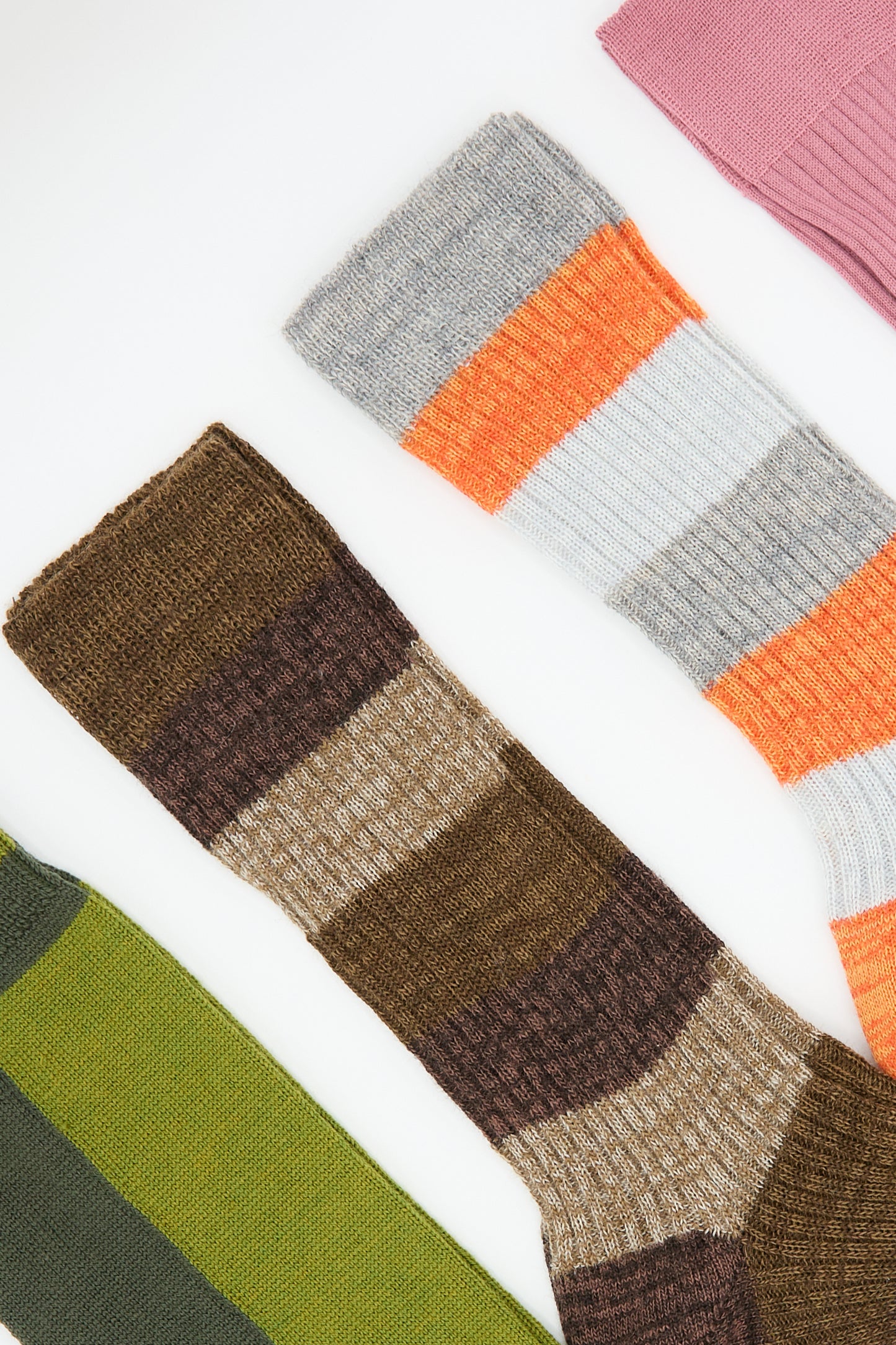 A photograph showcasing five pairs of Maria La Rosa's colorful, vertically arranged Long Socks in Khaki. These socks display an array of vibrant patterns and colors, such as pink, yellow, and grey stripes; brown and tan stripes; with a contrasting striped sock next to a green wool-blend sock.