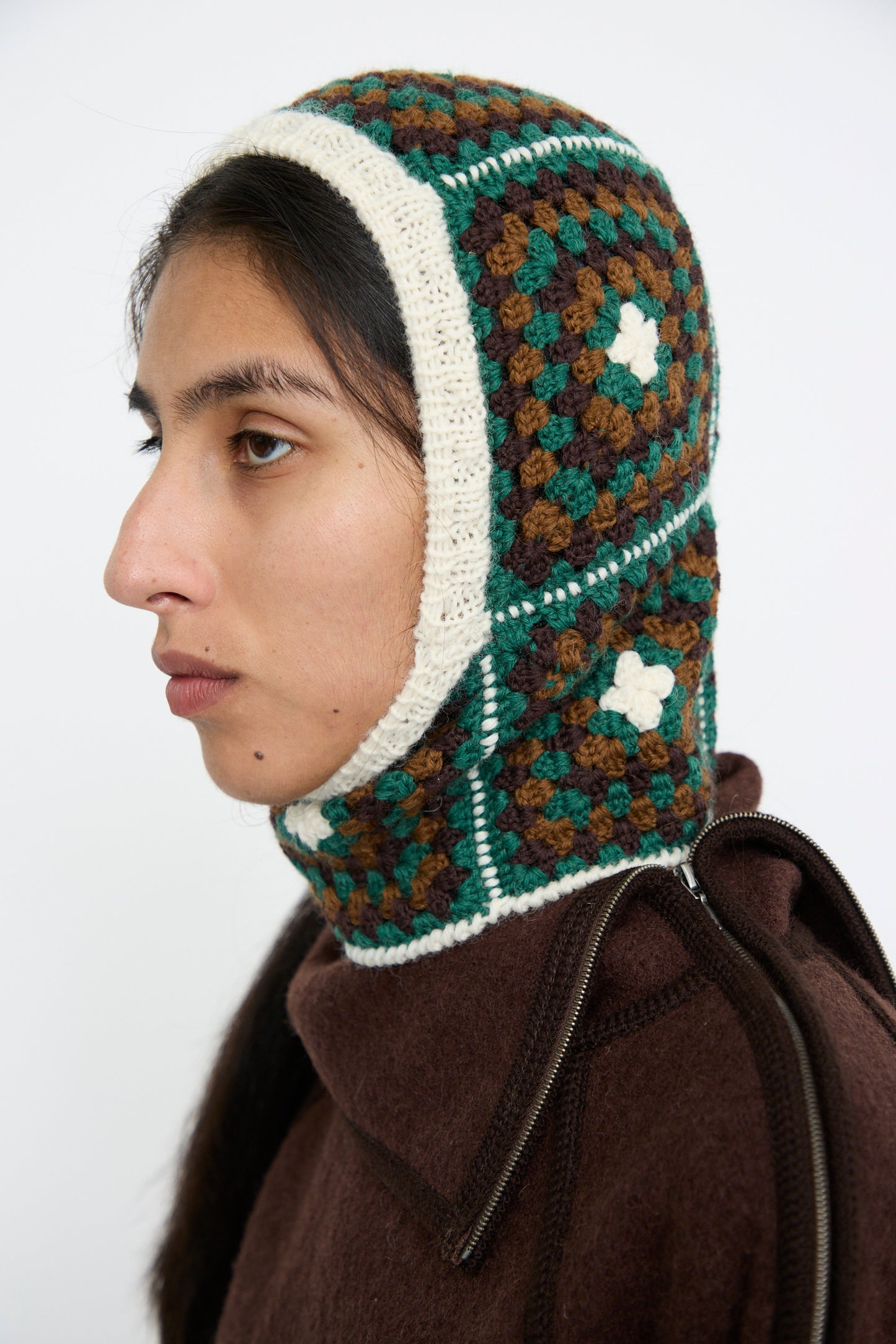 Side view of a person wearing the Balaclava in Emerald by Maria La Rosa, featuring a hand-knit geometric pattern in green, brown, and cream, against a plain background. 