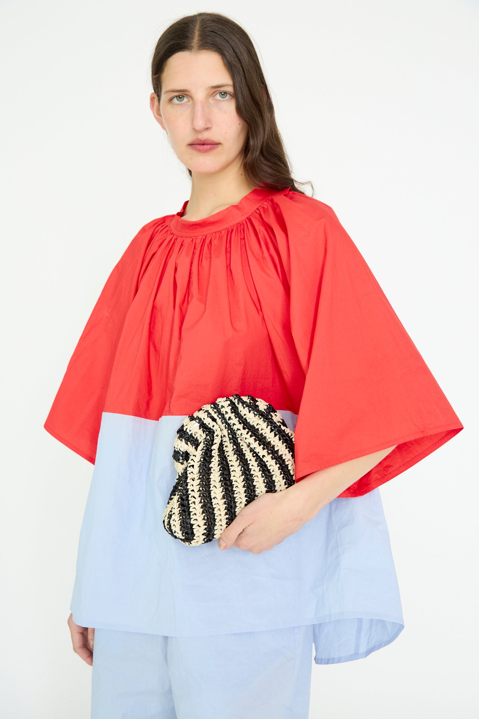A person in a red and blue top is holding a Maria La Rosa Crochet Mini Game Cromo Bag in Black, featuring a chain shoulder strap, against a plain background.
