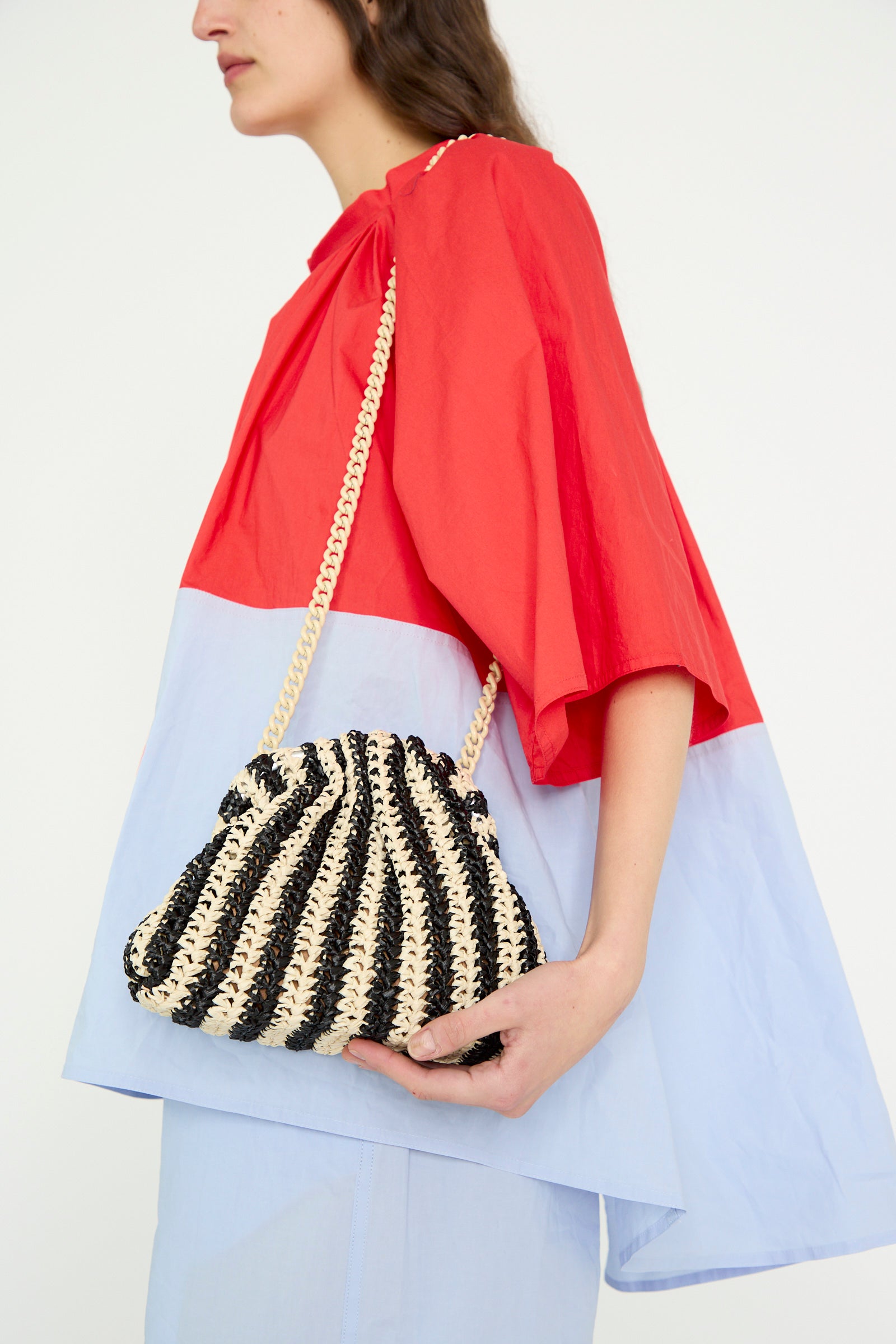 Dressed in a red and light blue outfit, a person carries the Crochet Mini Game Cromo Bag in Black by Maria La Rosa featuring a rope strap.