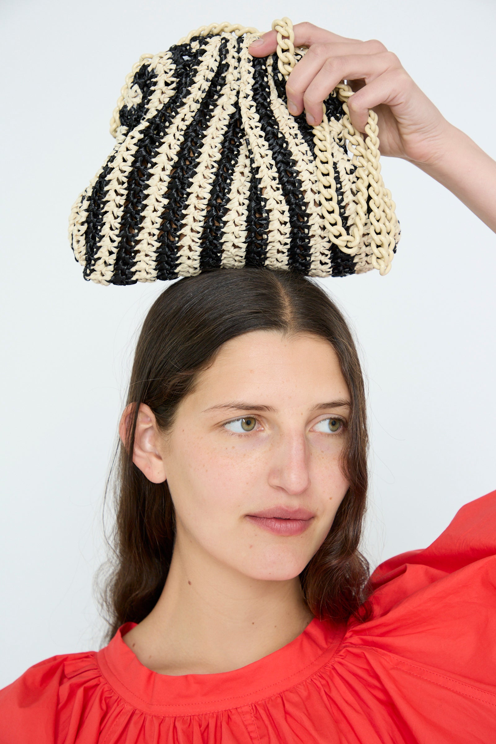 A person wearing a red top balances the Maria La Rosa Crochet Mini Game Cromo Bag in Black on their head against a plain background.