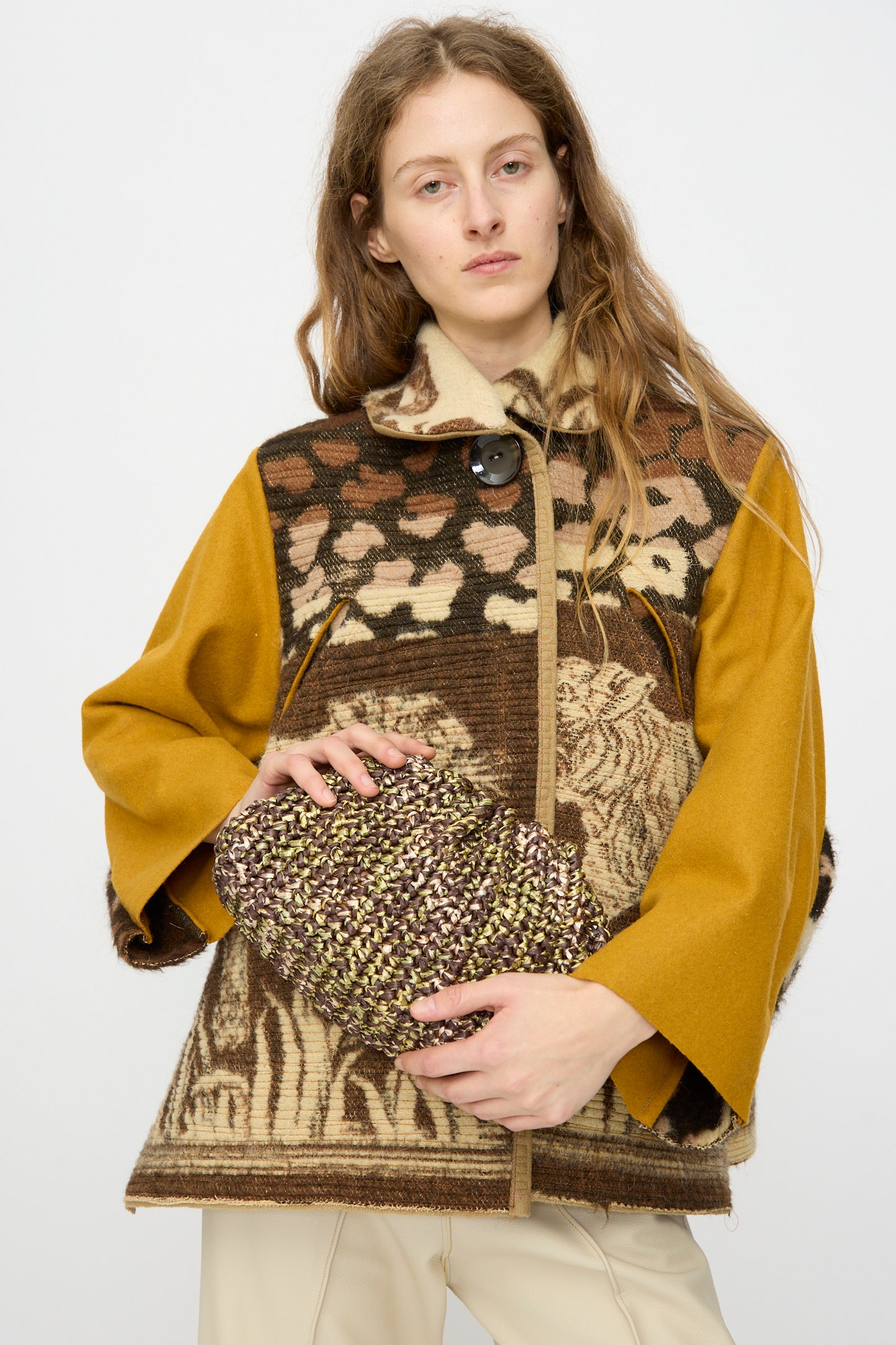 A person holds the Maria La Rosa Earth Game Crochet Bag in Natural against a plain white background, wearing a patterned brown and yellow jacket.