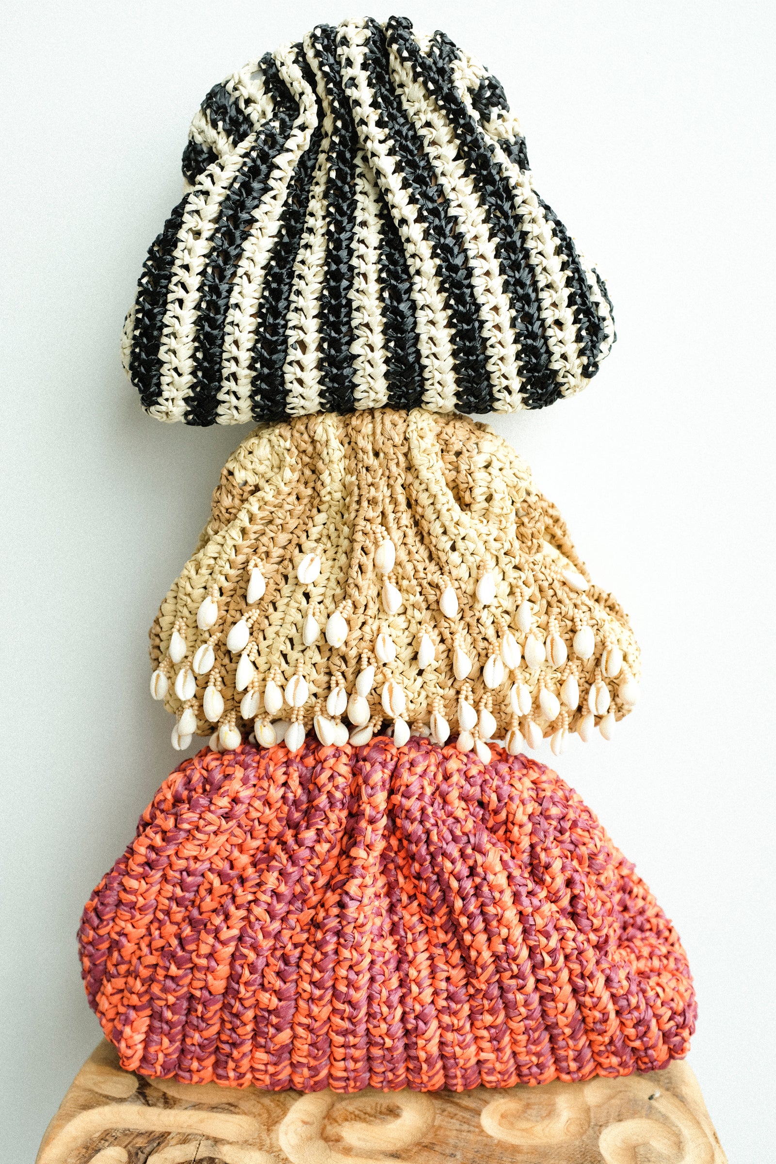 Stack of three knitted bags from Maria La Rosa in black, beige, and pink on a light gray background
