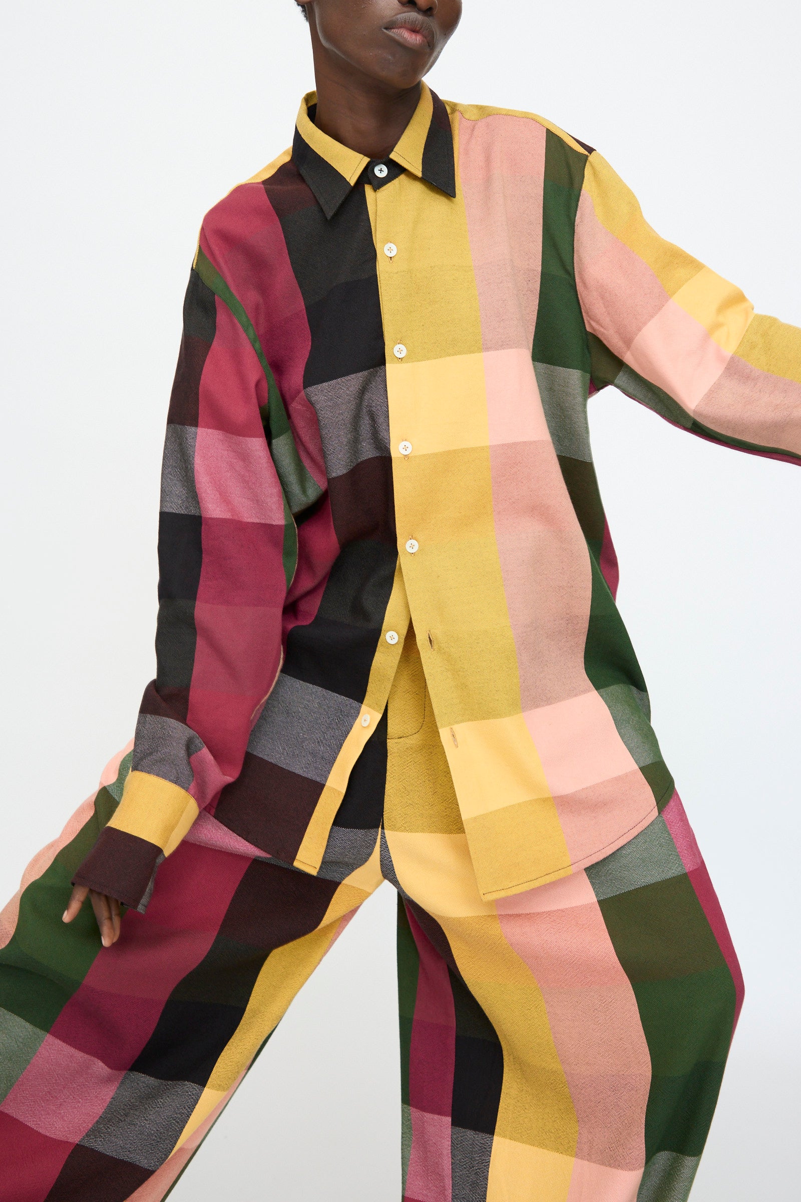 A person wears the Marrakshi Life Button Down Shirt in Plaid Multi, featuring a relaxed, oversized cotton blend and bold checkered patterns in yellow, pink, green, burgundy, and black, set against a plain background.