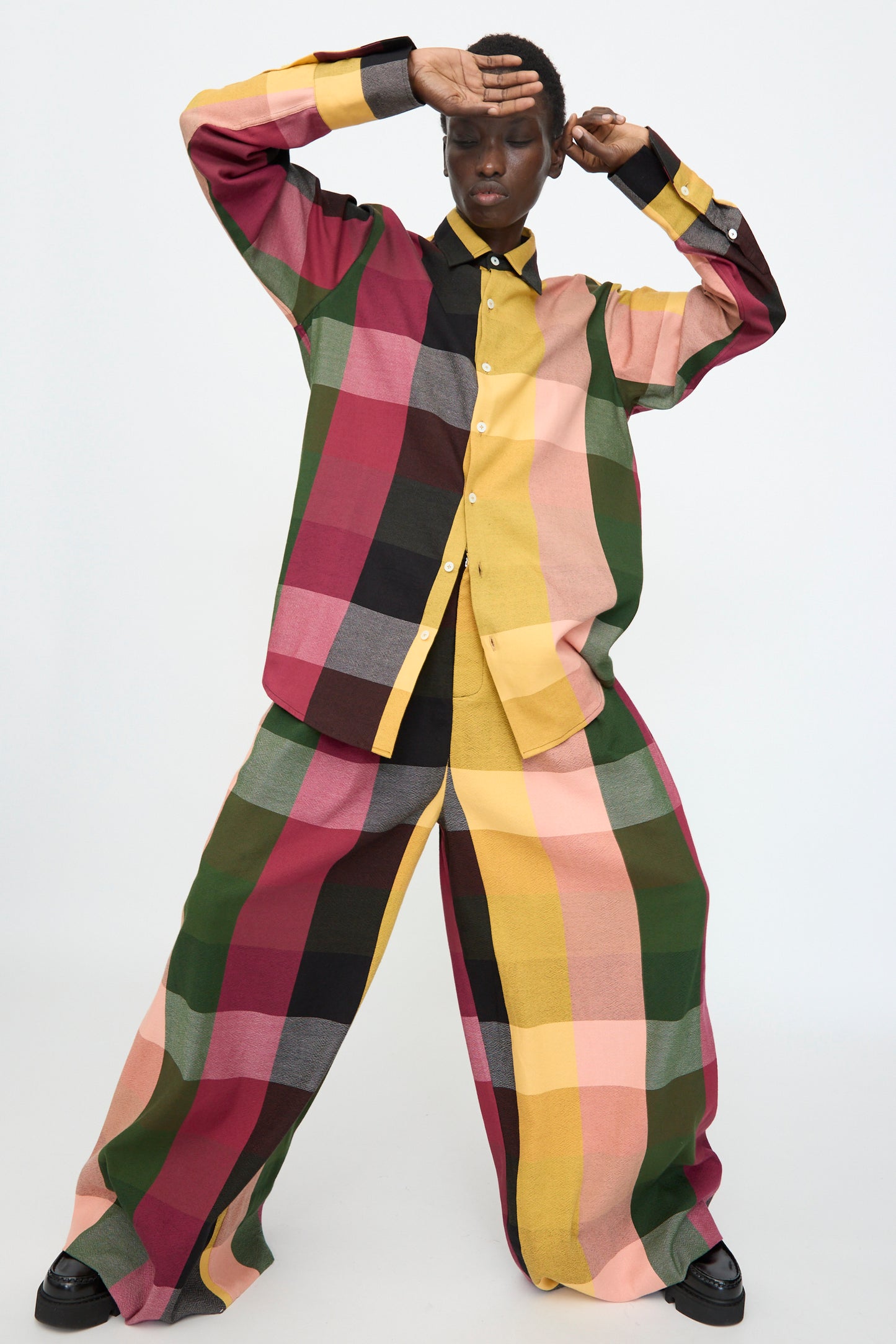 A person in the Marrakshi Life Button Down Shirt in Plaid Multi and matching wide-leg pants poses with one hand raised to their forehead against a plain background.