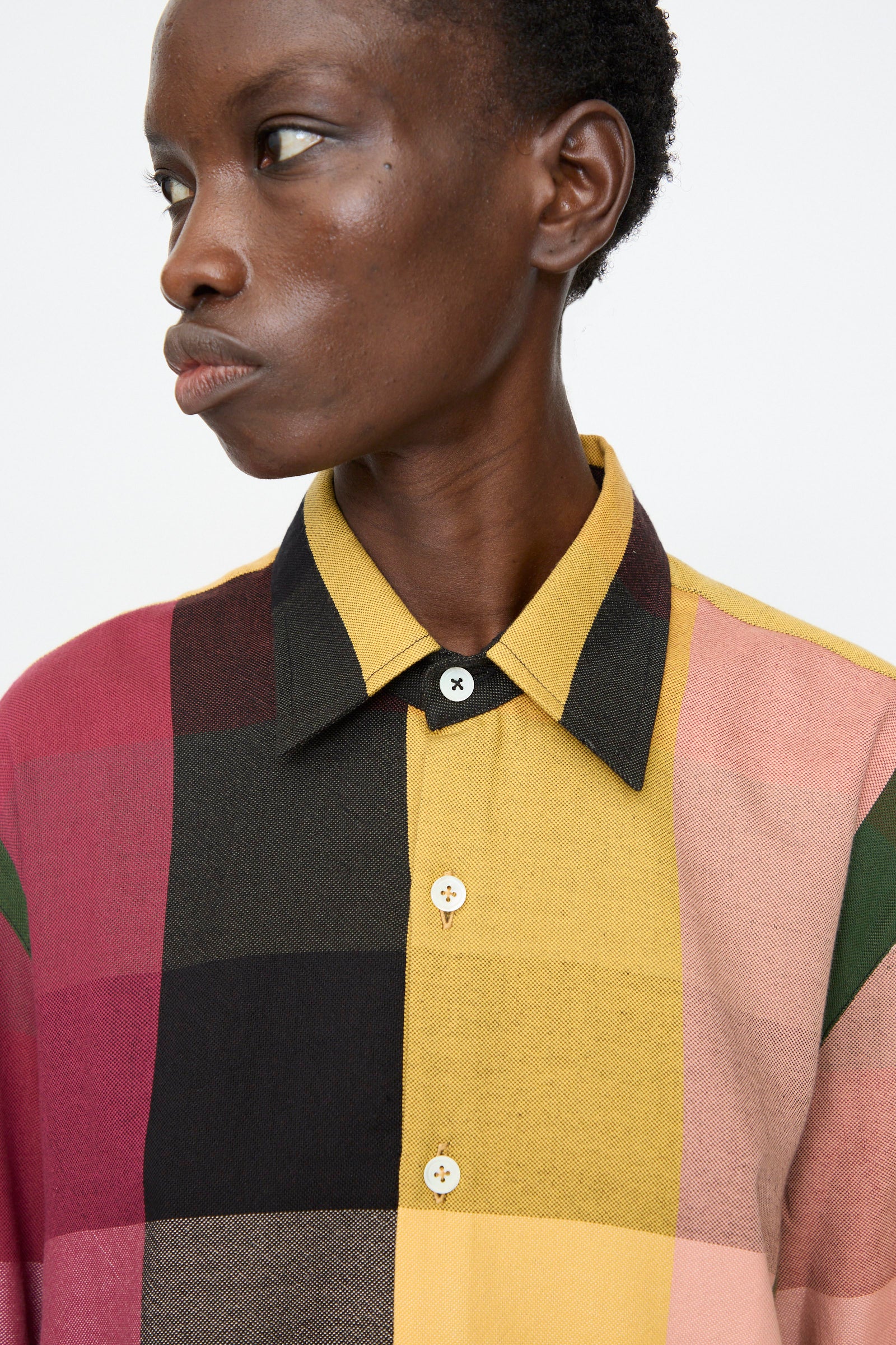 A person wearing the Marrakshi Life Button Down Shirt in Plaid Multi, featuring a relaxed fit and bold multicolored checks, looks left against a plain background.