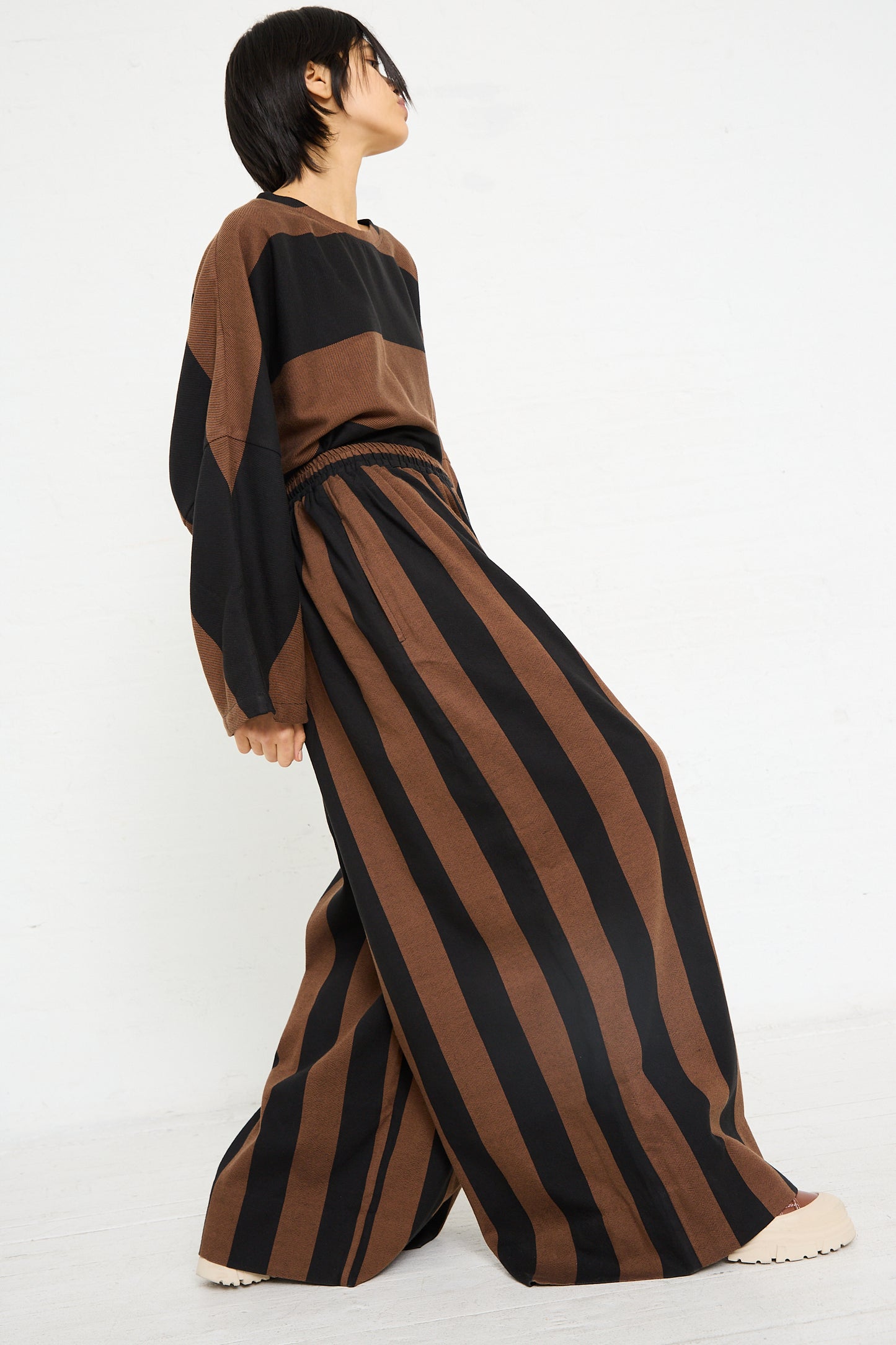 Woman modeling a Marrakshi Life Drawstring Pleated Pant in Black and Brown Stripe with a drawstring closure, and a loose-fitting top.