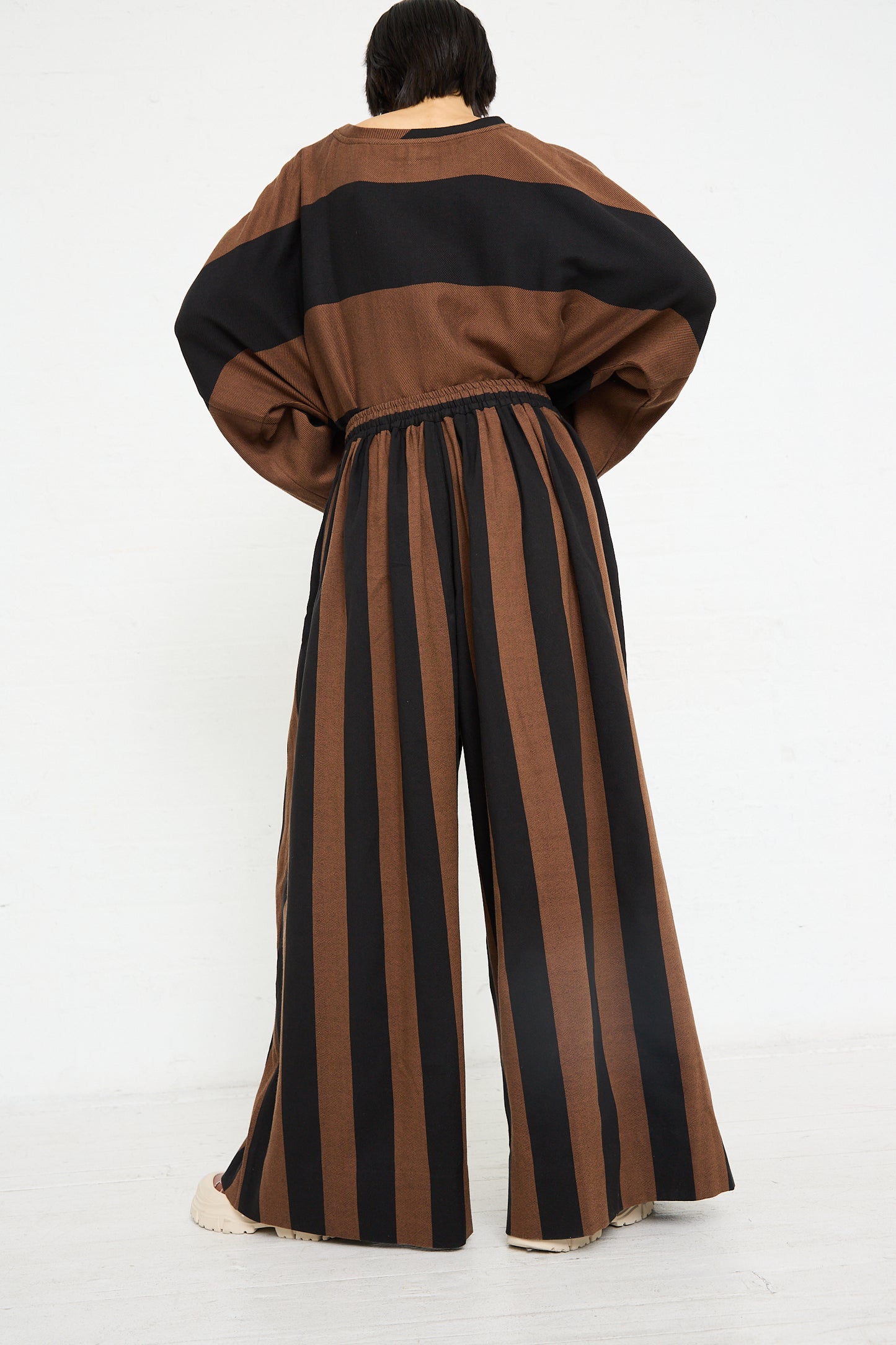 Woman seen from behind, wearing Marrakshi Life's Drawstring Pleated Pant in Black and Brown Stripe with puffed sleeves.
