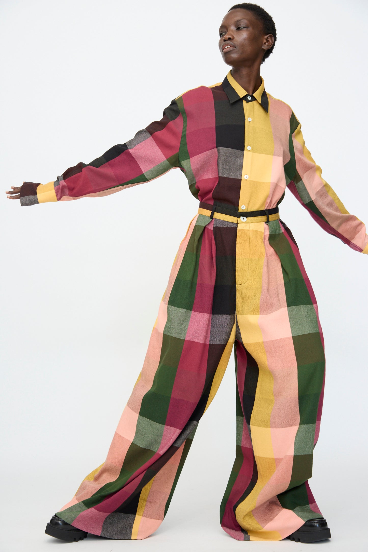 Model wears the Marrakshi Life High Waisted Pleated Trouser in Plaid Multi—cotton trousers in red, pink, green, yellow, and black—standing against a plain white background.
