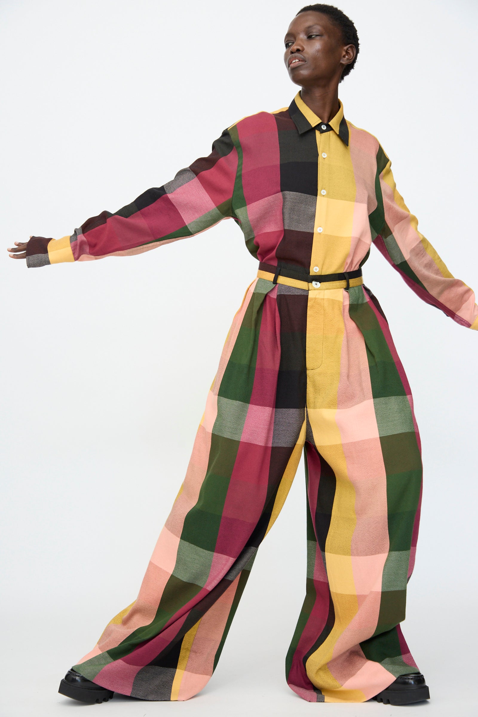 Model wears the Marrakshi Life High Waisted Pleated Trouser in Plaid Multi—cotton trousers in red, pink, green, yellow, and black—standing against a plain white background.