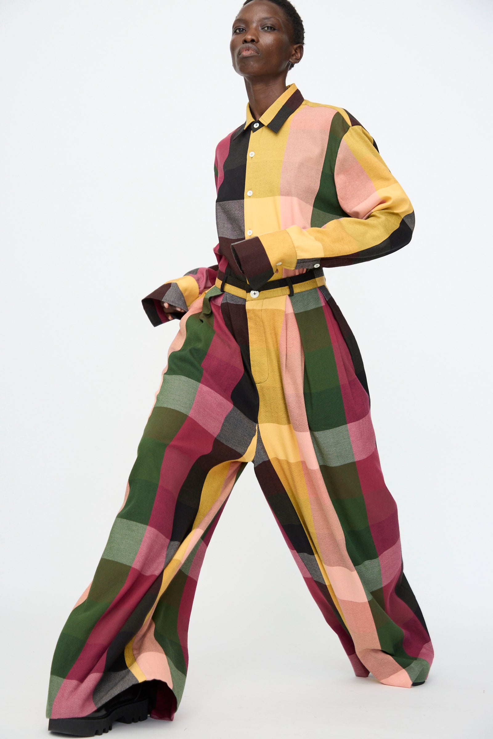 A person wearing Marrakshi Life's High Waisted Pleated Trouser in Plaid Multi, paired with a matching long-sleeve shirt, walks against a plain white background.