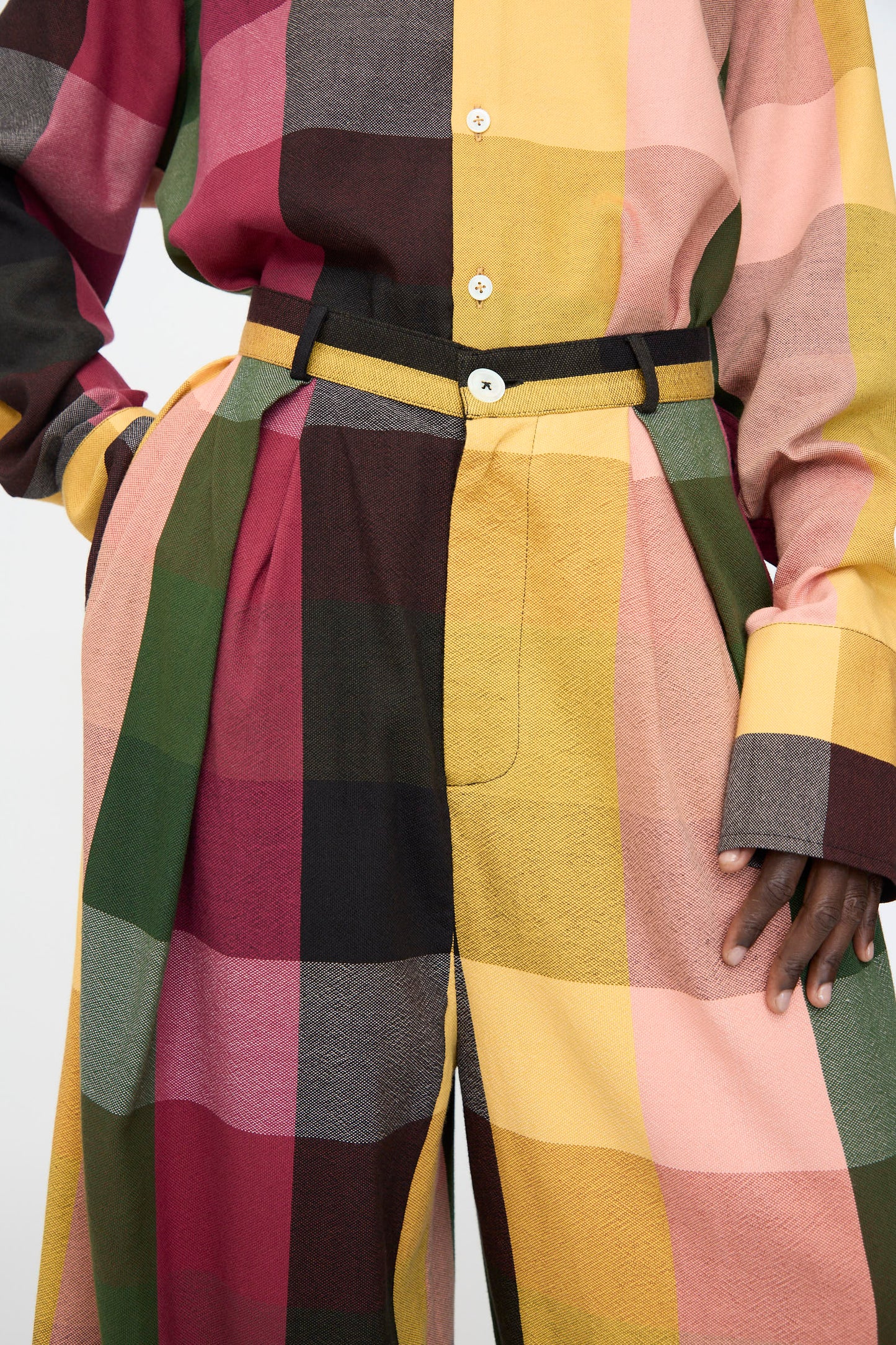 A person wearing a loose cotton shirt and Marrakshi Life’s High Waisted Pleated Trouser in Plaid Multi, featuring a wide-leg fit and large plaid pattern in yellow, pink, green, and maroon.