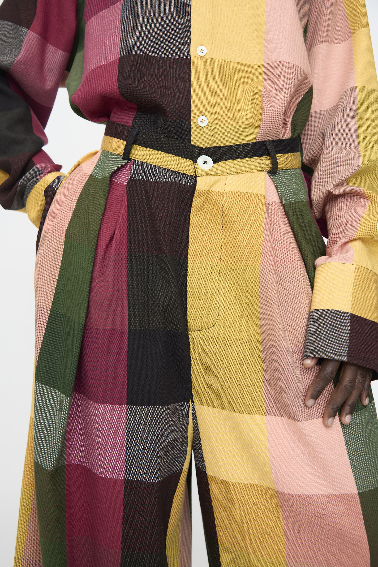 A person wearing a loose cotton shirt and Marrakshi Life’s High Waisted Pleated Trouser in Plaid Multi, featuring a wide-leg fit and large plaid pattern in yellow, pink, green, and maroon.