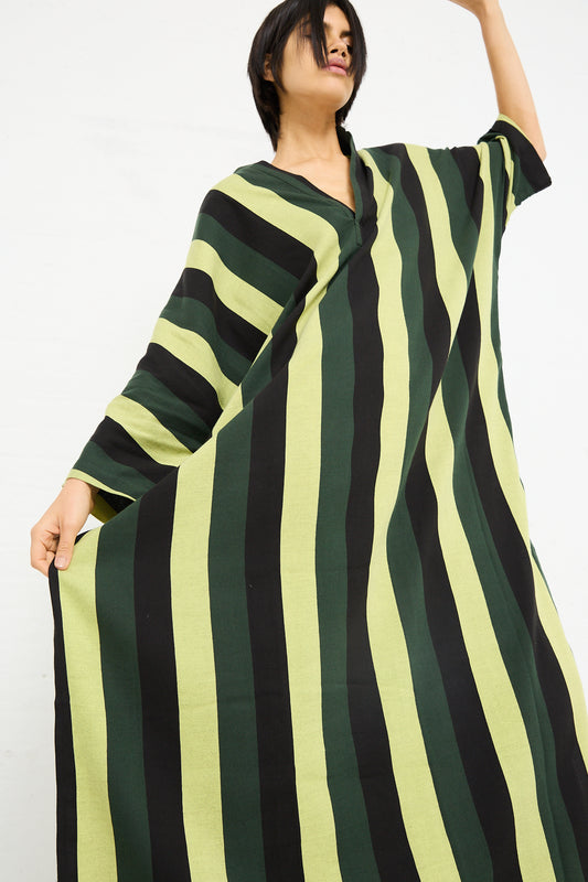 Woman in a Marrakshi Life Nero Collar Caftan in Green Stripe posing with her arm raised against a white background.