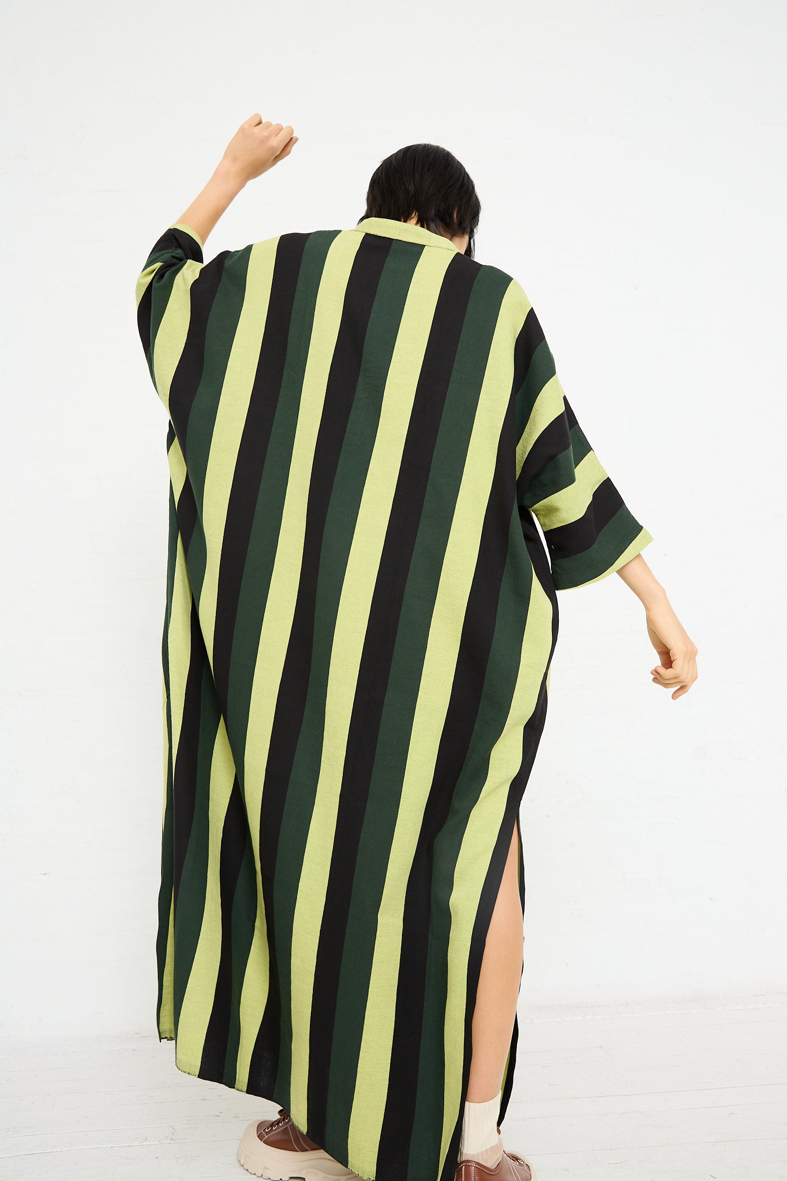 A person in a Nero Collar Caftan in Green Stripe from Marrakshi Life with an oversized fit posing with one arm raised.