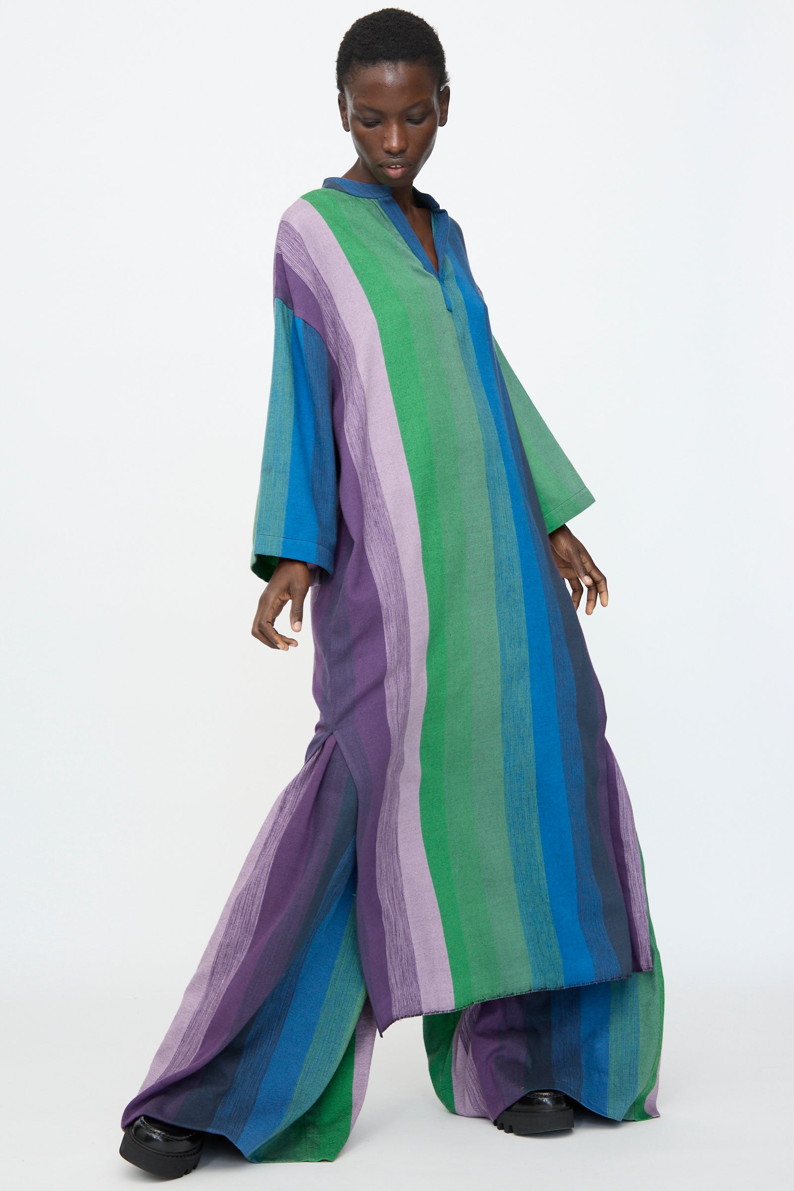 A model wears Marrakshi Life’s Nero Collar Caftan in Stripe Multi, an oversized design with wide legs and sleeves and vertical green, blue, and purple stripes, posing against a plain white background.