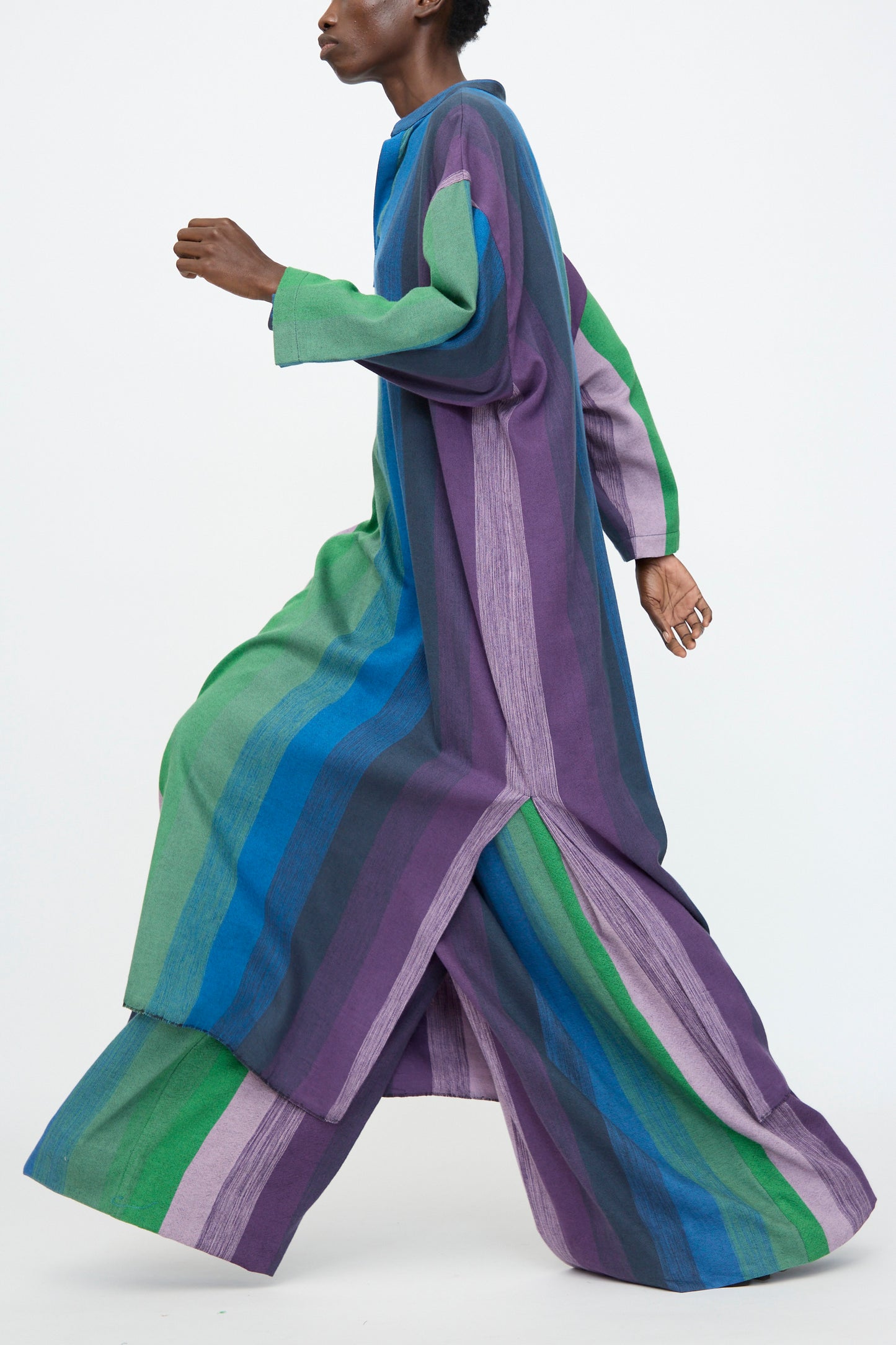 A person in profile wears the Marrakshi Life Nero Collar Caftan in Stripe Multi—a long, loose-fitting cotton caftan with vertical green, blue, and purple stripes—against a plain background.