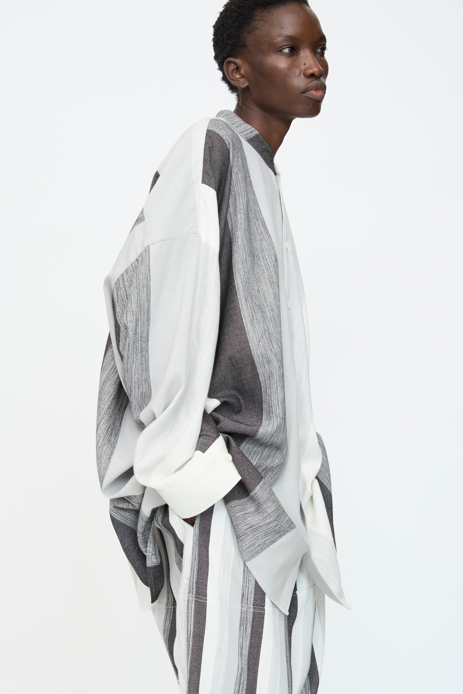 A person stands against a plain white background wearing the Marrakshi Life Nero Collar Oversized Shirt in Grey Stripe with matching pants.