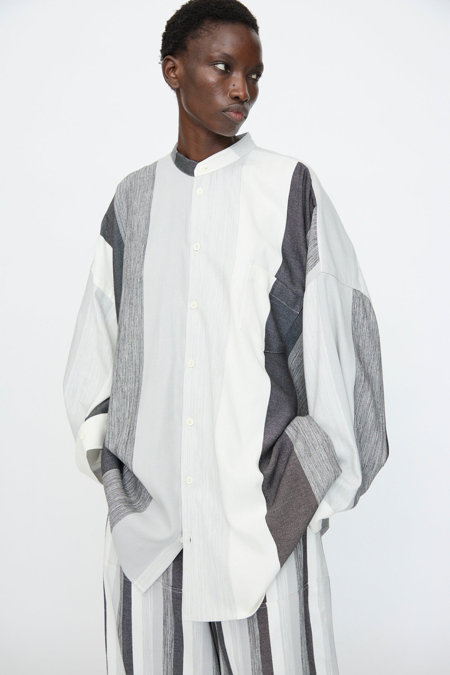 A person wears the Marrakshi Life Nero Collar Oversized Shirt in Grey Stripe—loose-fitting and boxy—with matching striped pants, standing against a plain white background.