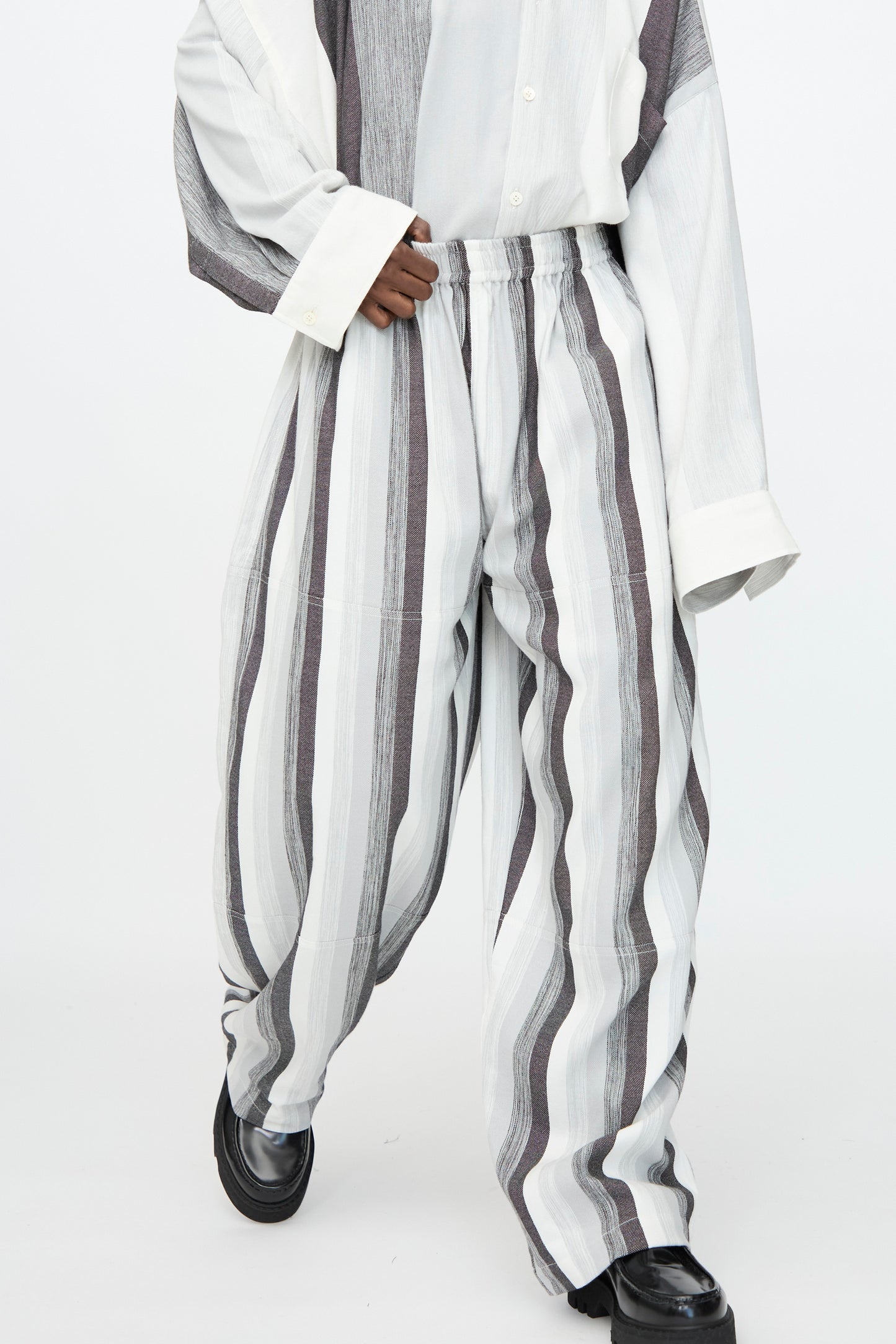 Wearing Marrakshi Life’s Parachute Pant in Grey Stripe with a matching oversized shirt and black shoes, set against a plain background.