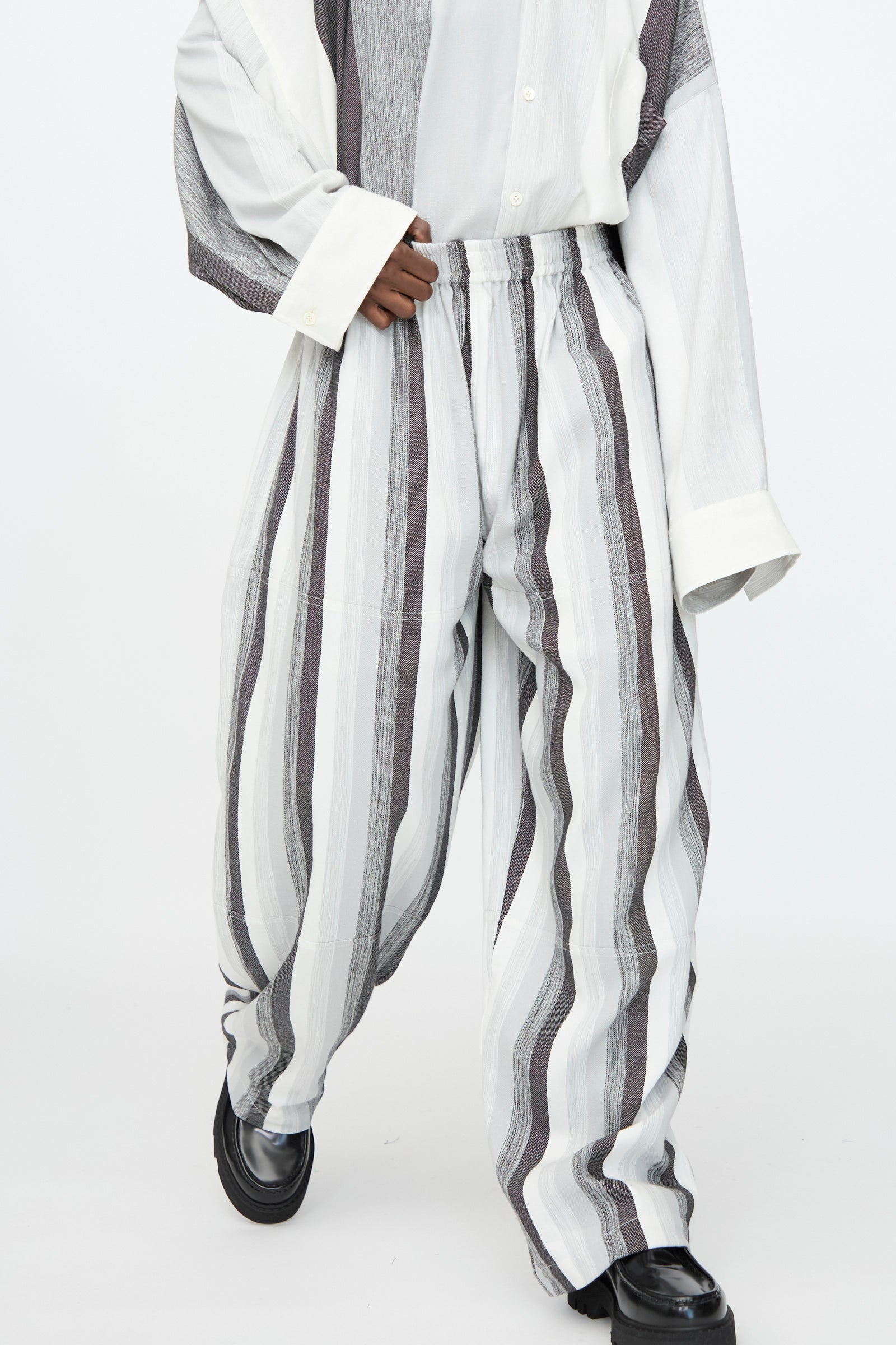 Wearing Marrakshi Life’s Parachute Pant in Grey Stripe with a matching oversized shirt and black shoes, set against a plain background.