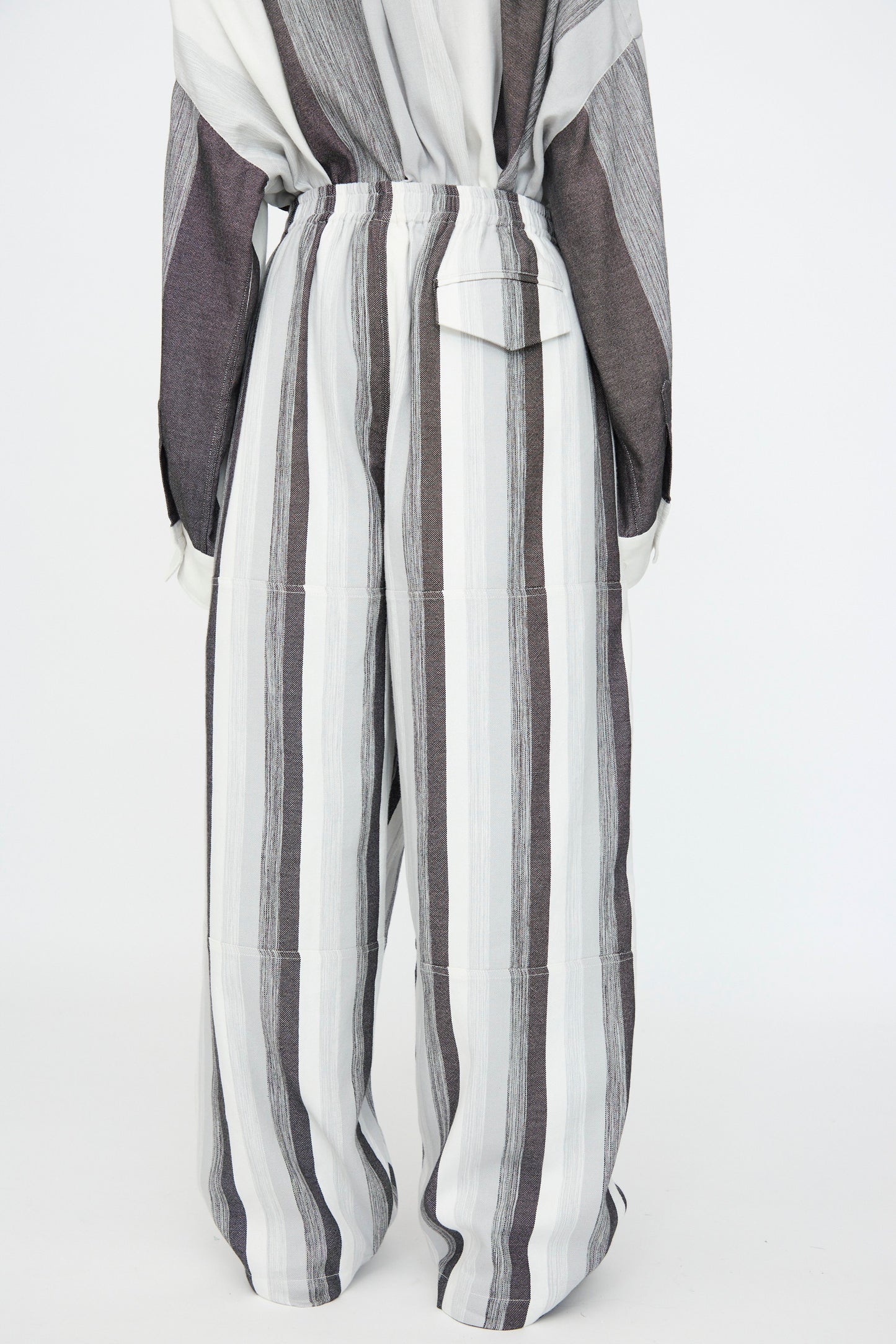 A person wears the Marrakshi Life Parachute Pant in Grey Stripe—an oversized, high-waisted wide leg cotton pant with vertical white and grey stripes—photographed from the back against a plain white background.