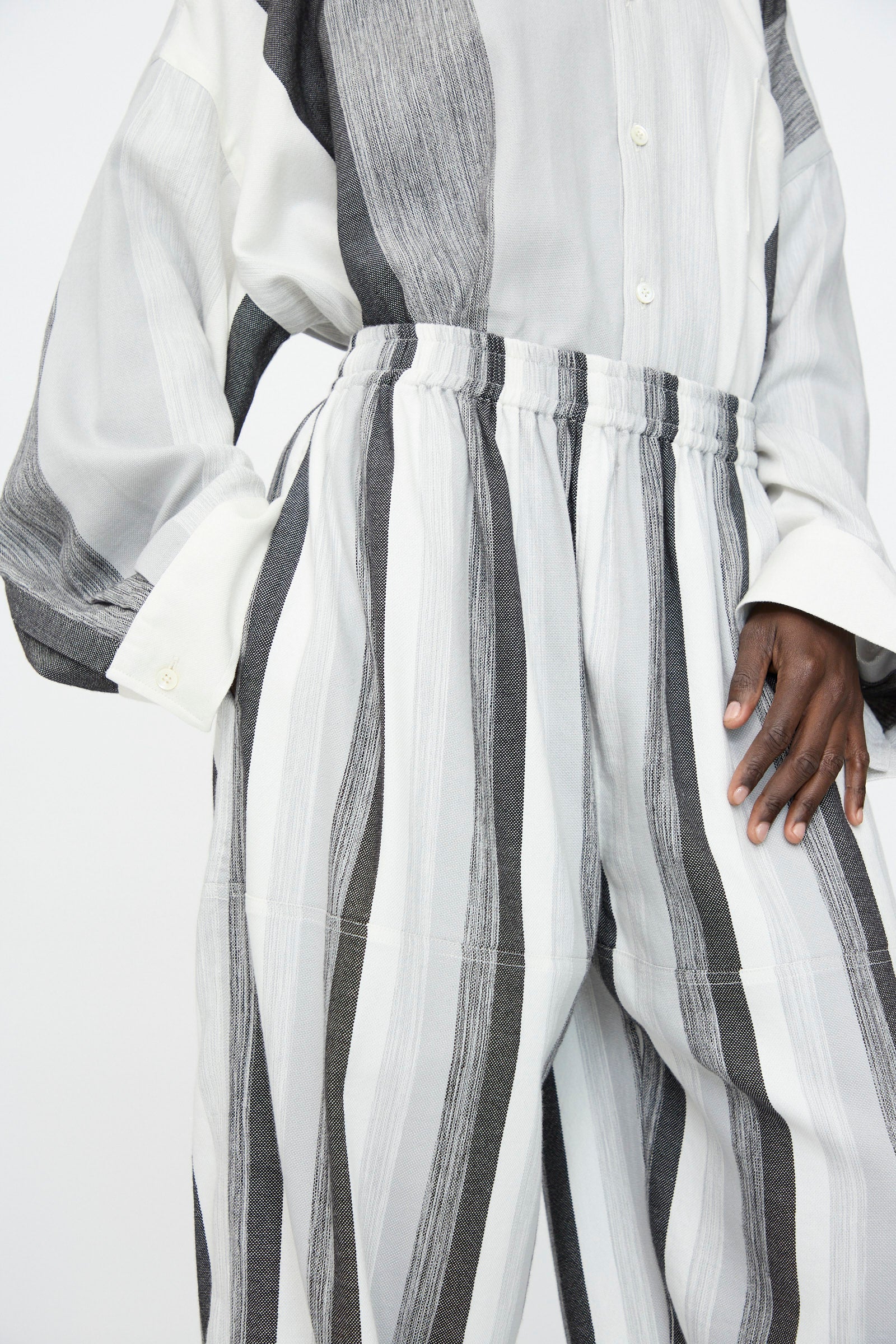 A person wearing an oversized, long-sleeved shirt with Marrakshi Life’s Parachute Pant in Grey Stripe—high-waisted, wide-leg pants crafted from striped black and white cotton.