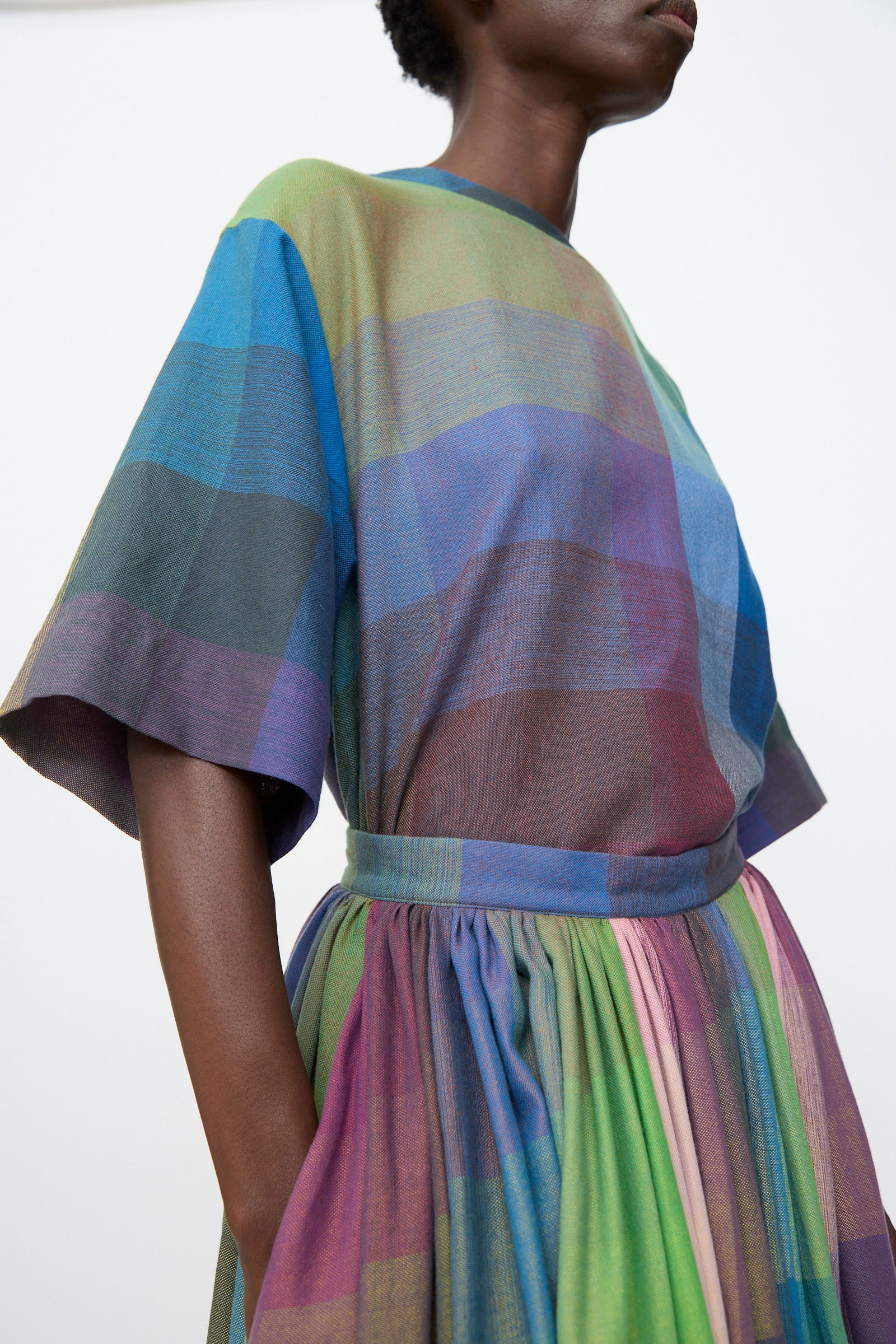 A person wears the Marrakshi Life Puffer Skirt in Plaid Multi, featuring a fitted waist and gathered skirt, standing against a plain background.