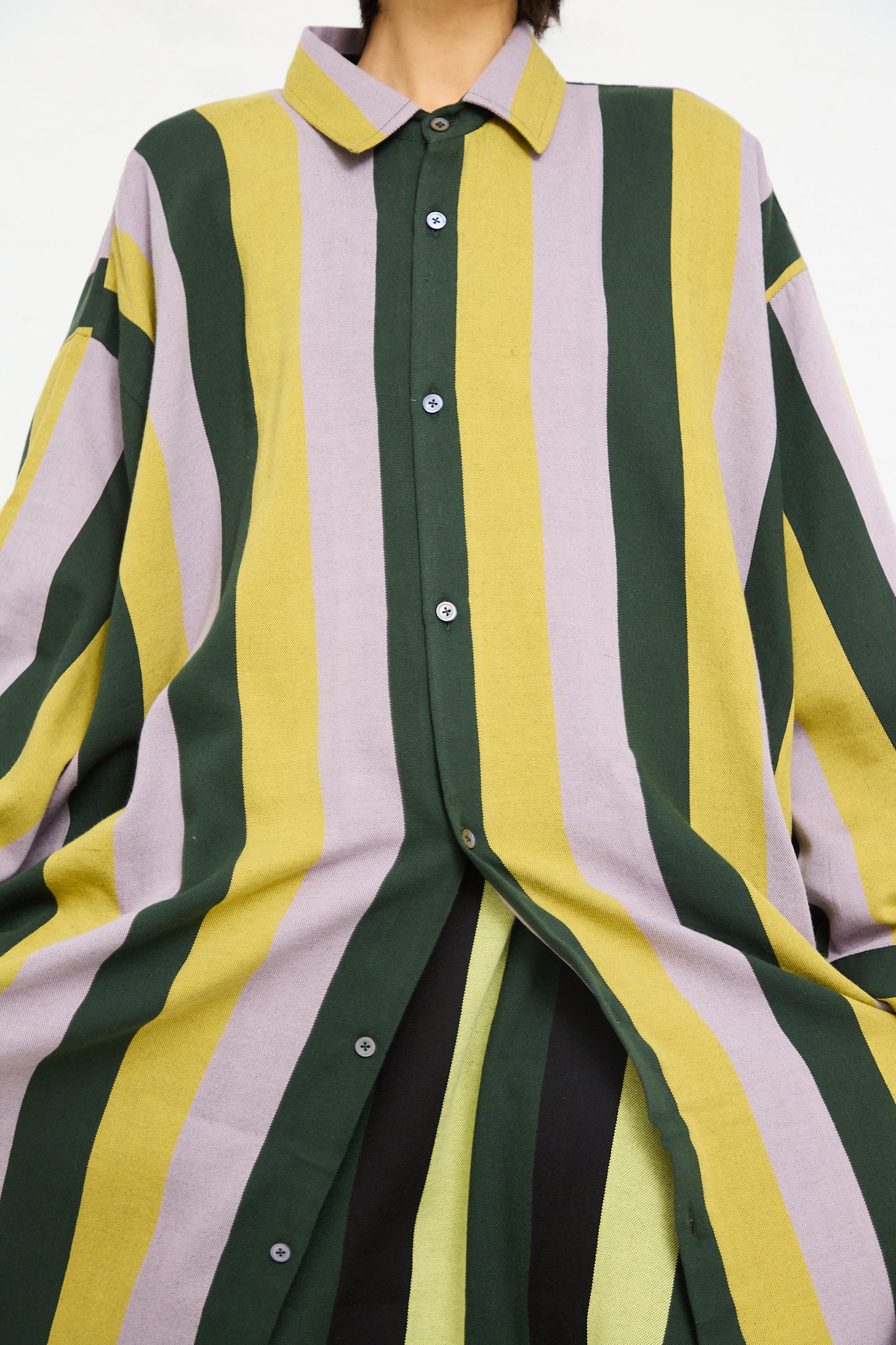 A person wearing a Marrakshi Life Small Collar Oversized Shirt in Stripe with a combination of yellow, green, and white colors, featuring a buttoned front and a collar.