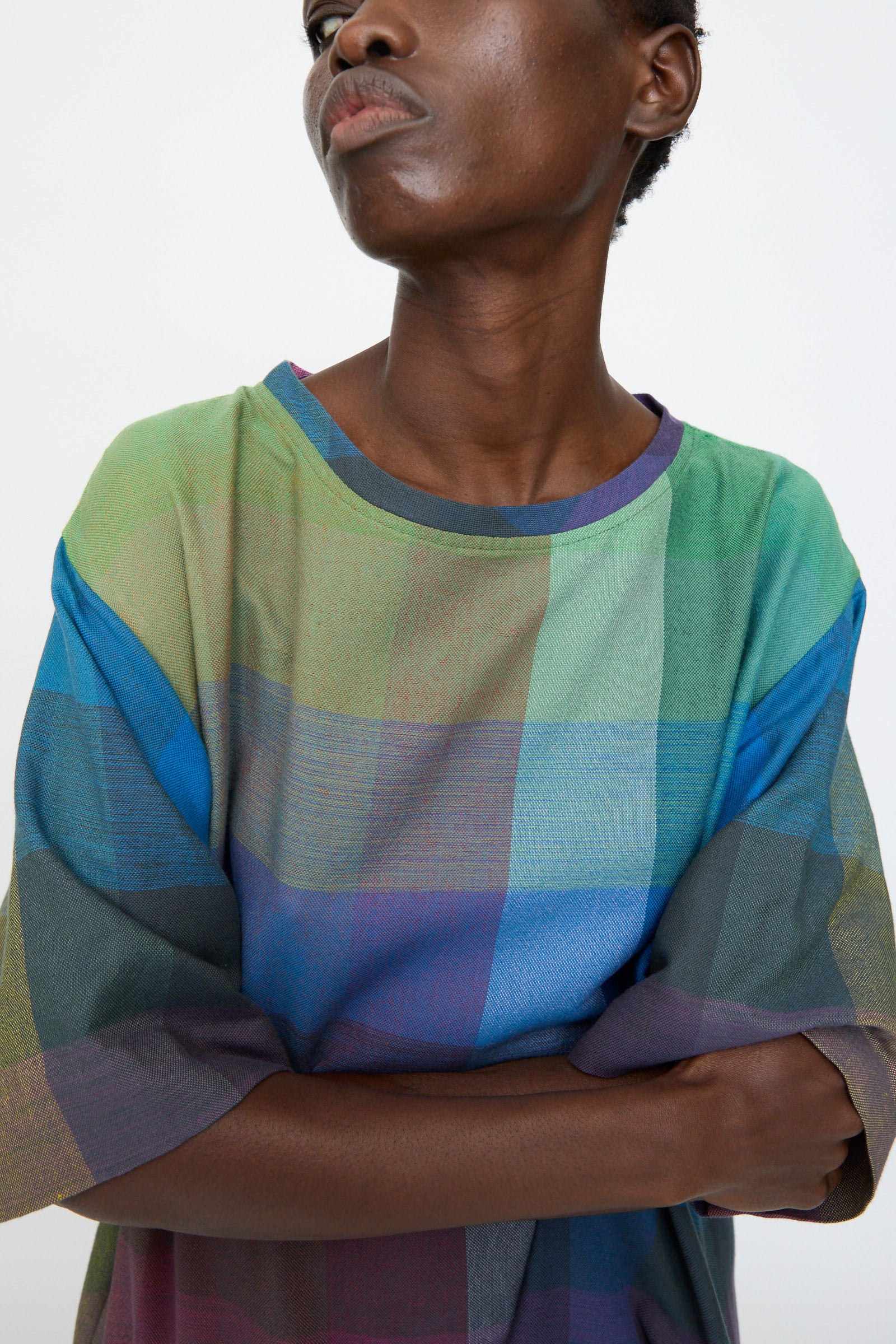 A person with short hair crosses their arms while wearing the Marrakshi Life T Shirt Dress in Plaid Multi against a plain background.