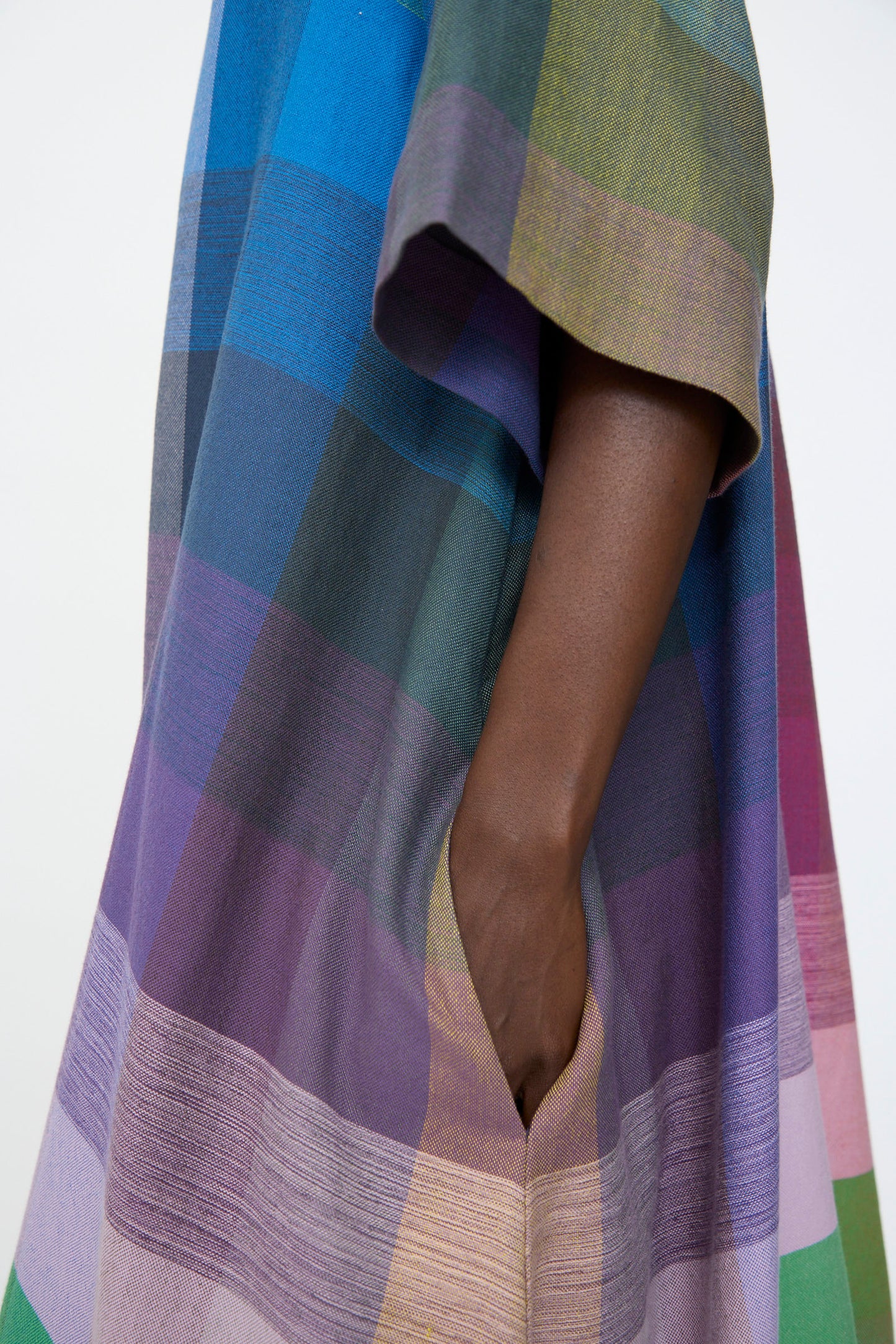 A person with dark skin rests their hand in the pocket of a loose-fitting, oversized T Shirt Dress in Plaid Multi by Marrakshi Life.