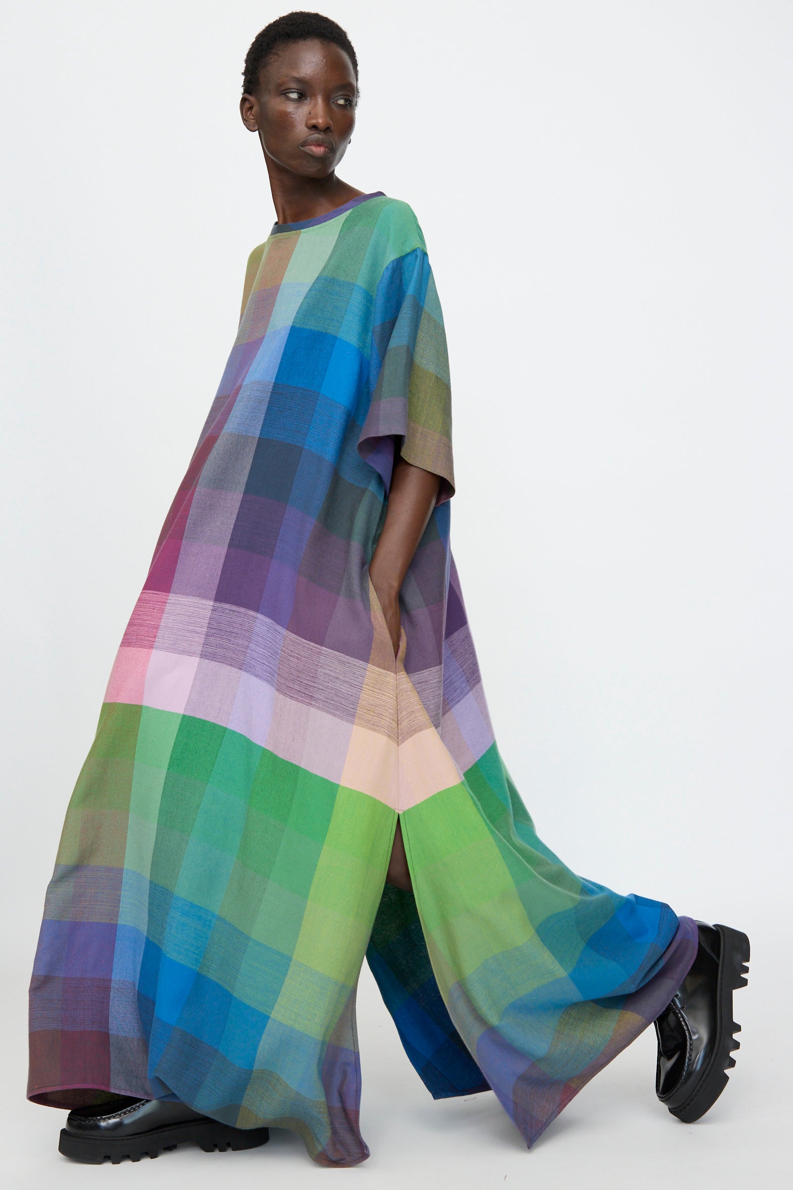 Model wears the Marrakshi Life T Shirt Dress in Plaid Multi—an oversized, colorful maxi style—paired with black chunky shoes, walking against a plain white background.