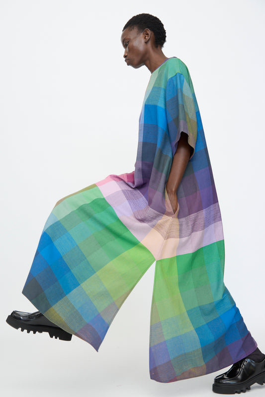 A person in profile wears the Marrakshi Life T Shirt Dress in Plaid Multi with black shoes, walking against a plain white background.