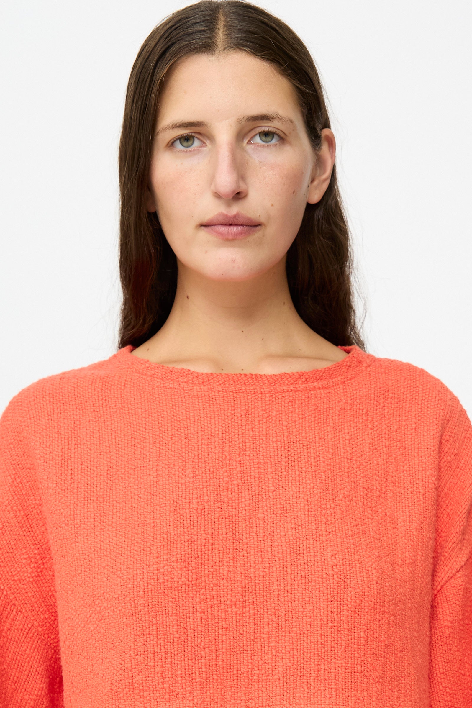 A person with long brown hair, facing forward against a plain white background, is wearing Marrakshi Life’s Cropped T-Shirt in Burnt Orange Flamme.