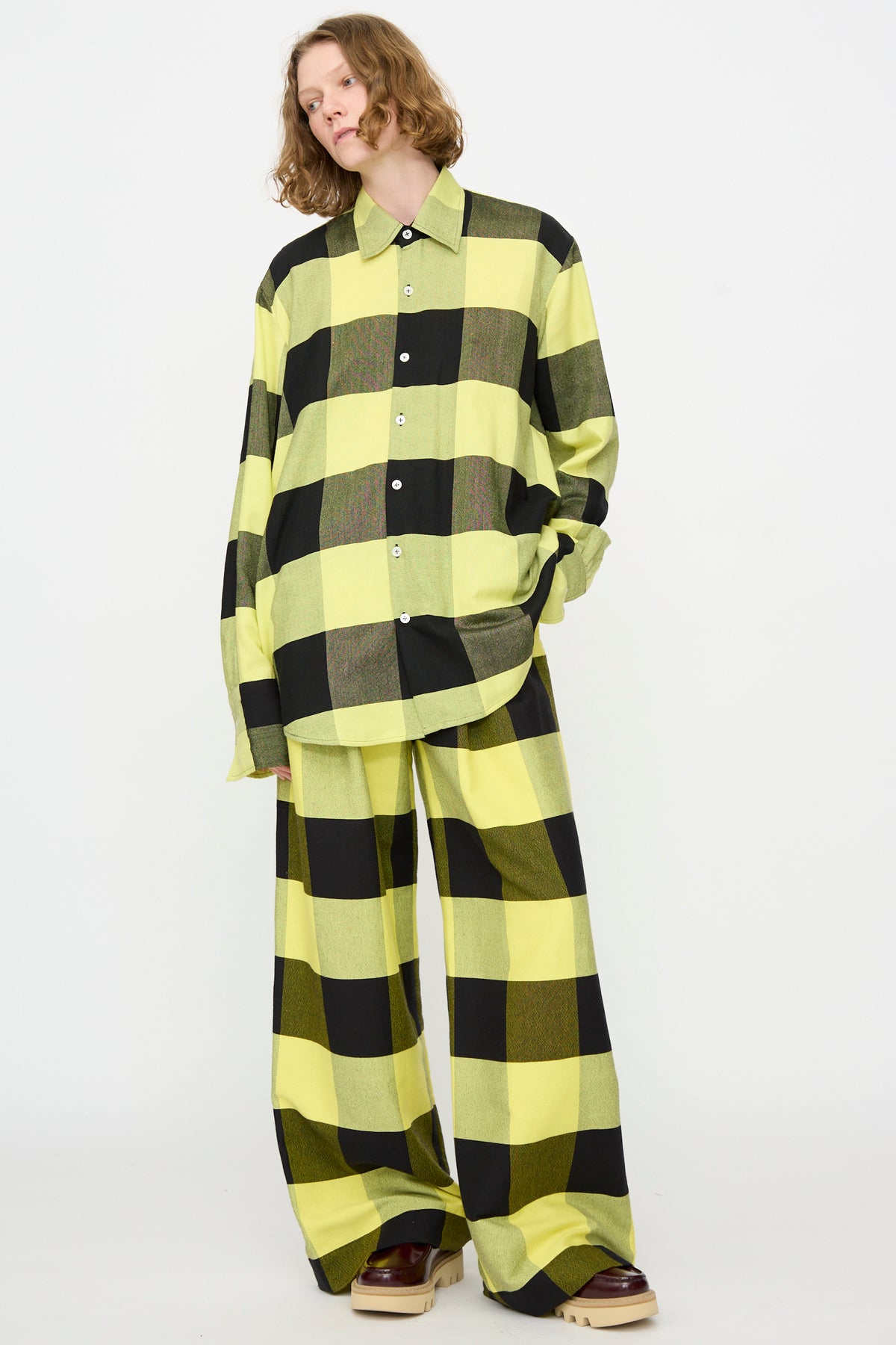 A person wearing Marrakshi Life’s The French Cuff Shirt in Plaid Black and Sunny, paired with matching wide-leg pants, stands against a plain white background.