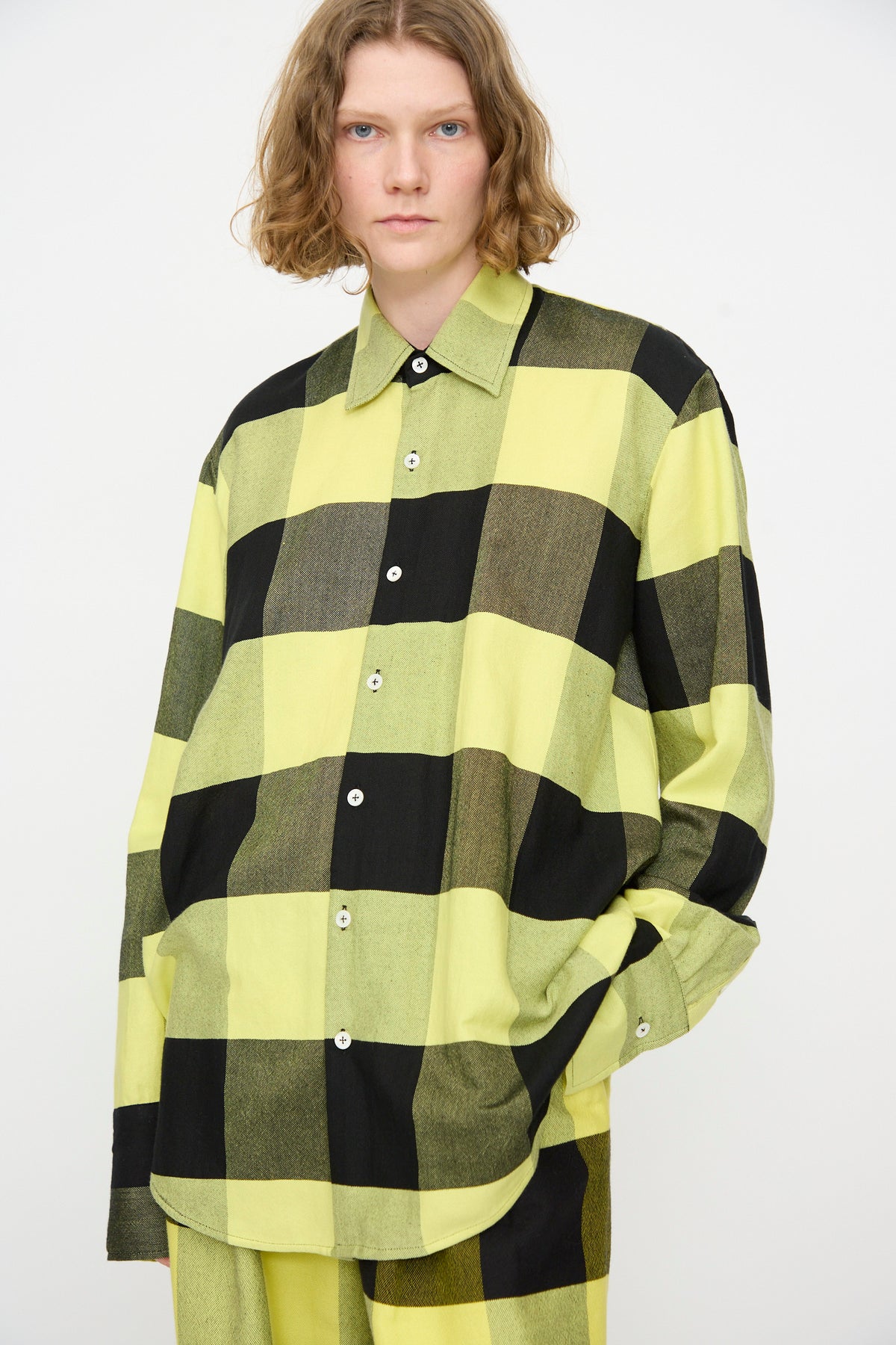 A person wearing Marrakshi Life’s The French Cuff Shirt in Plaid Black and Sunny, paired with matching pants, stands against a plain white background.